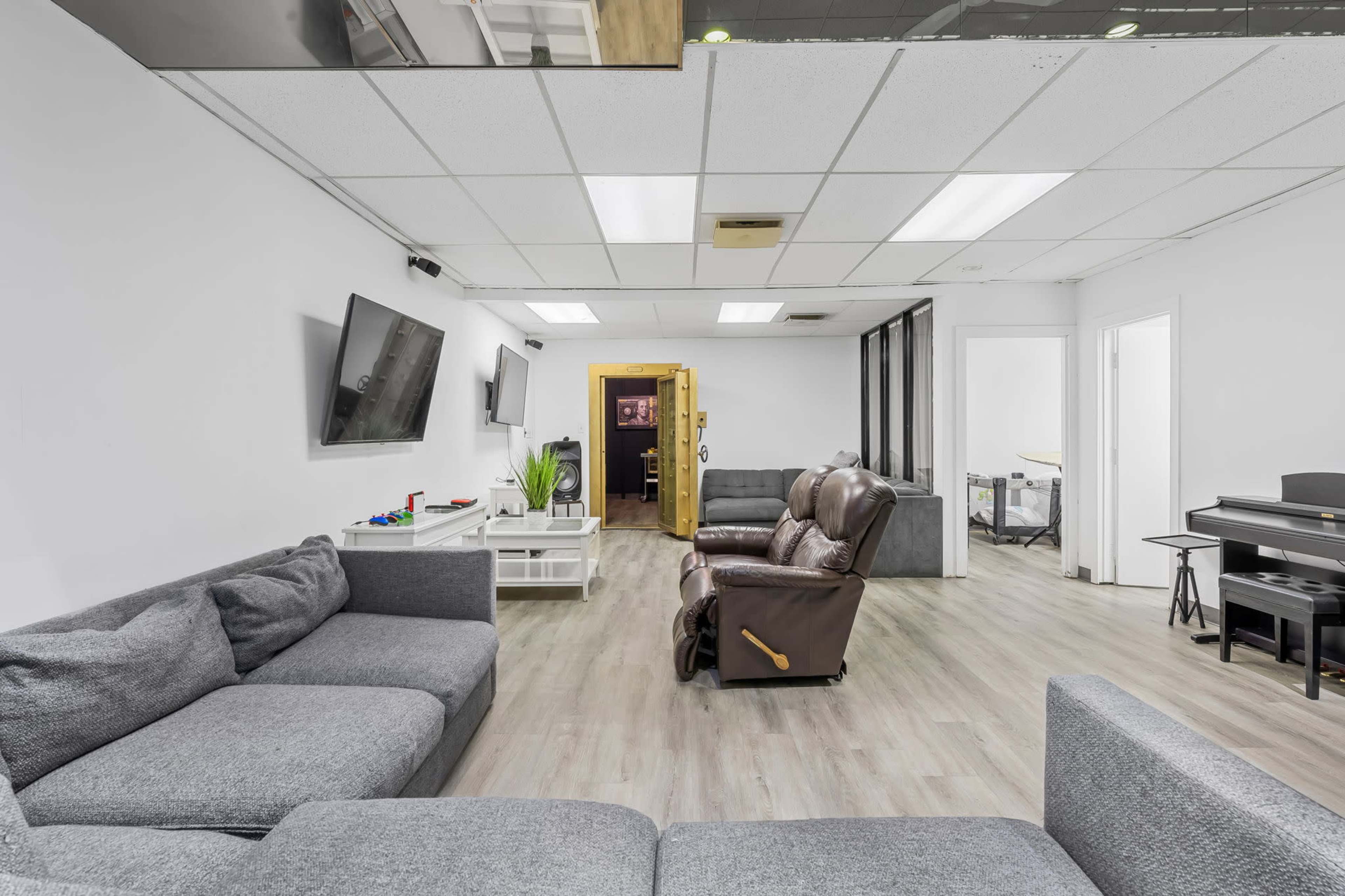 The image shows a modern office lounge area with gray sofas, a television on the wall, and a brown recliner chair.