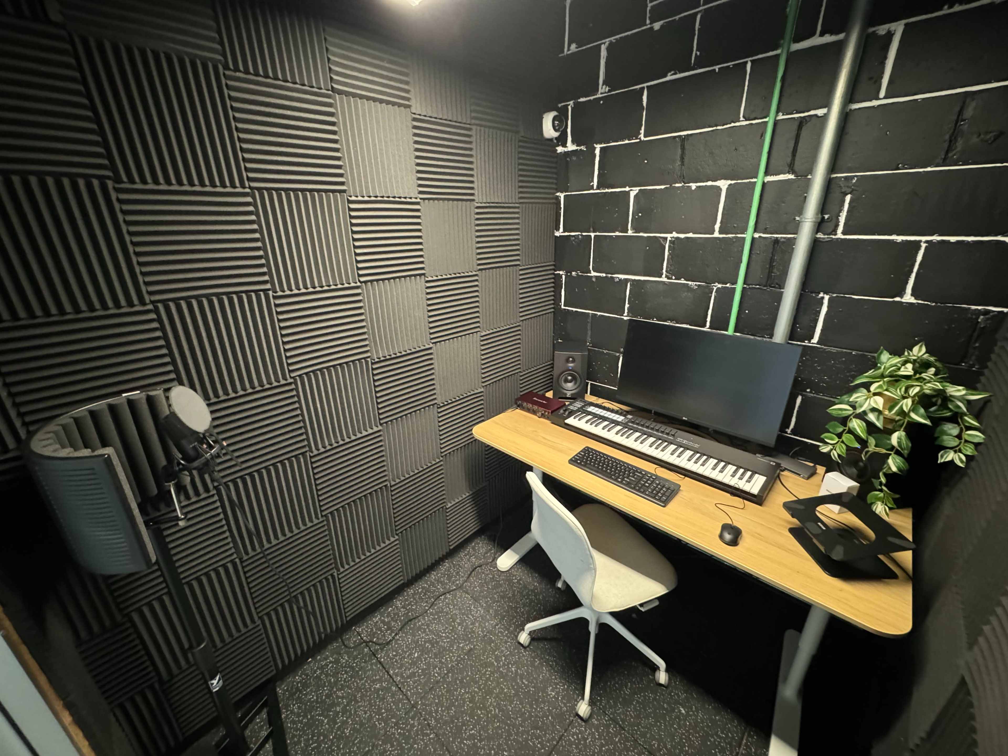 The image shows a soundproofed music production studio featuring a desk with a keyboard, monitor, microphone, and an office chair.