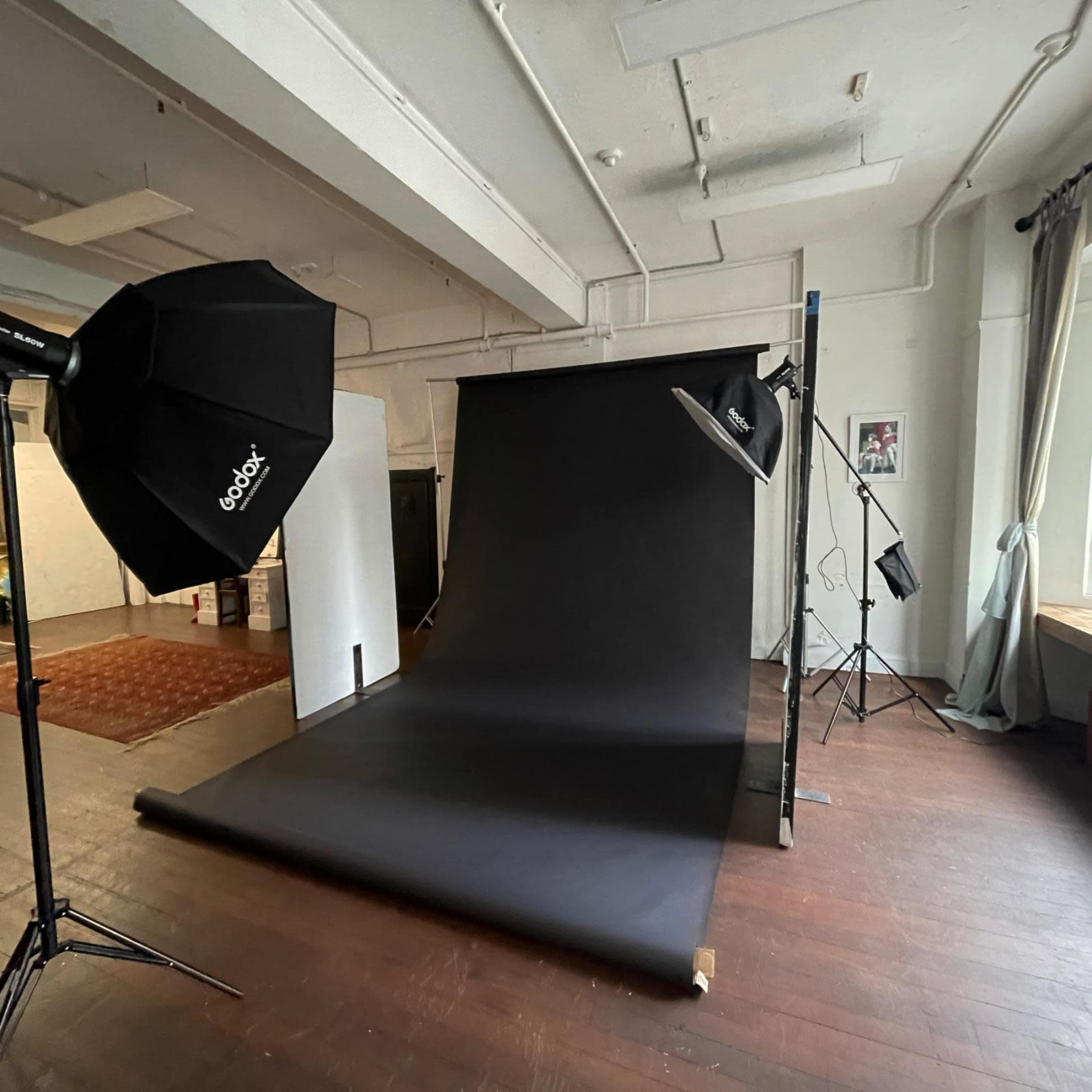 A photo studio with a black backdrop, lighting equipment, and wooden flooring.
