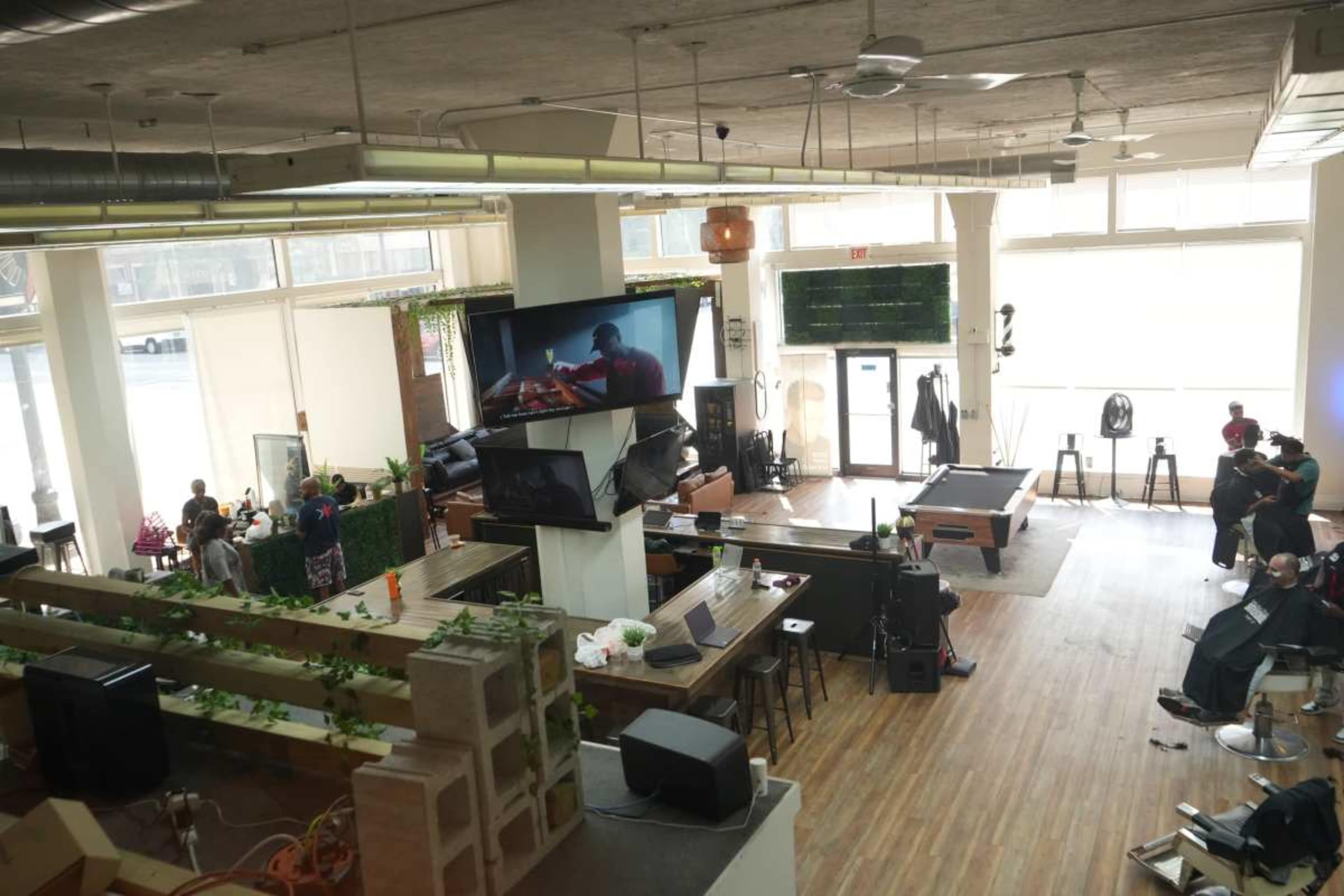 The image shows a spacious, modern indoor lounge area with seating, a pool table, and a bar, along with large windows and screens displaying a performance.