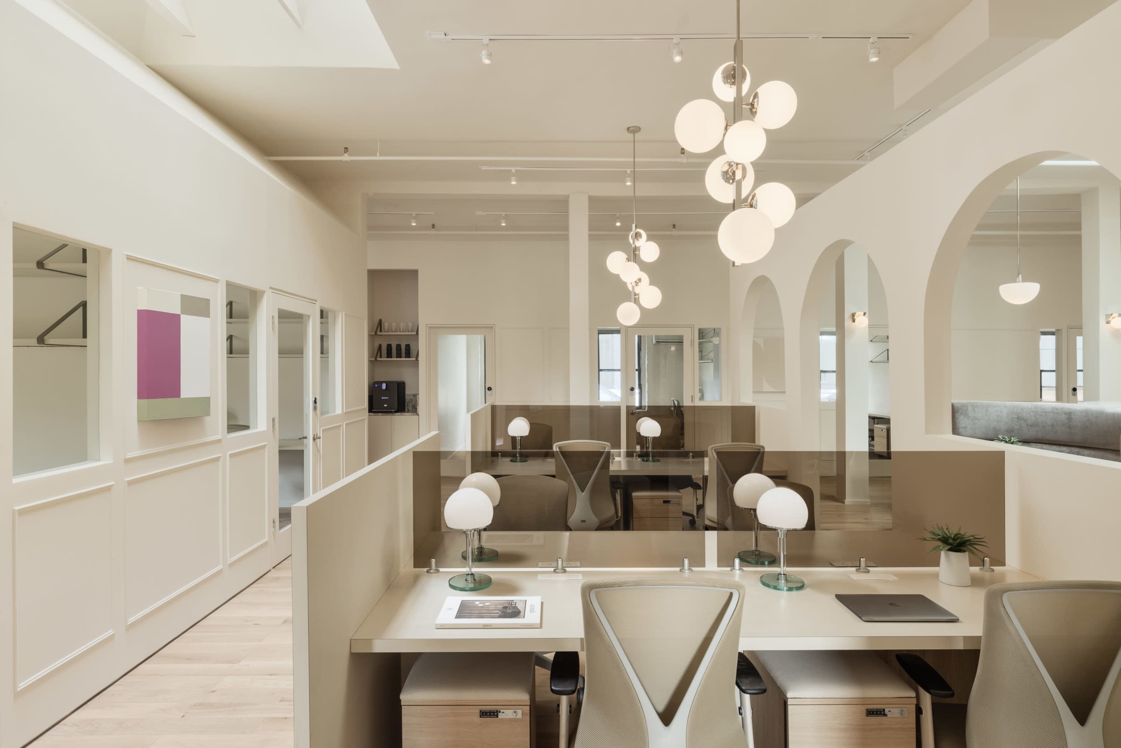 A modern office interior featuring light-colored walls, arched openings, and workstations with desk lamps arranged in a spacious layout.