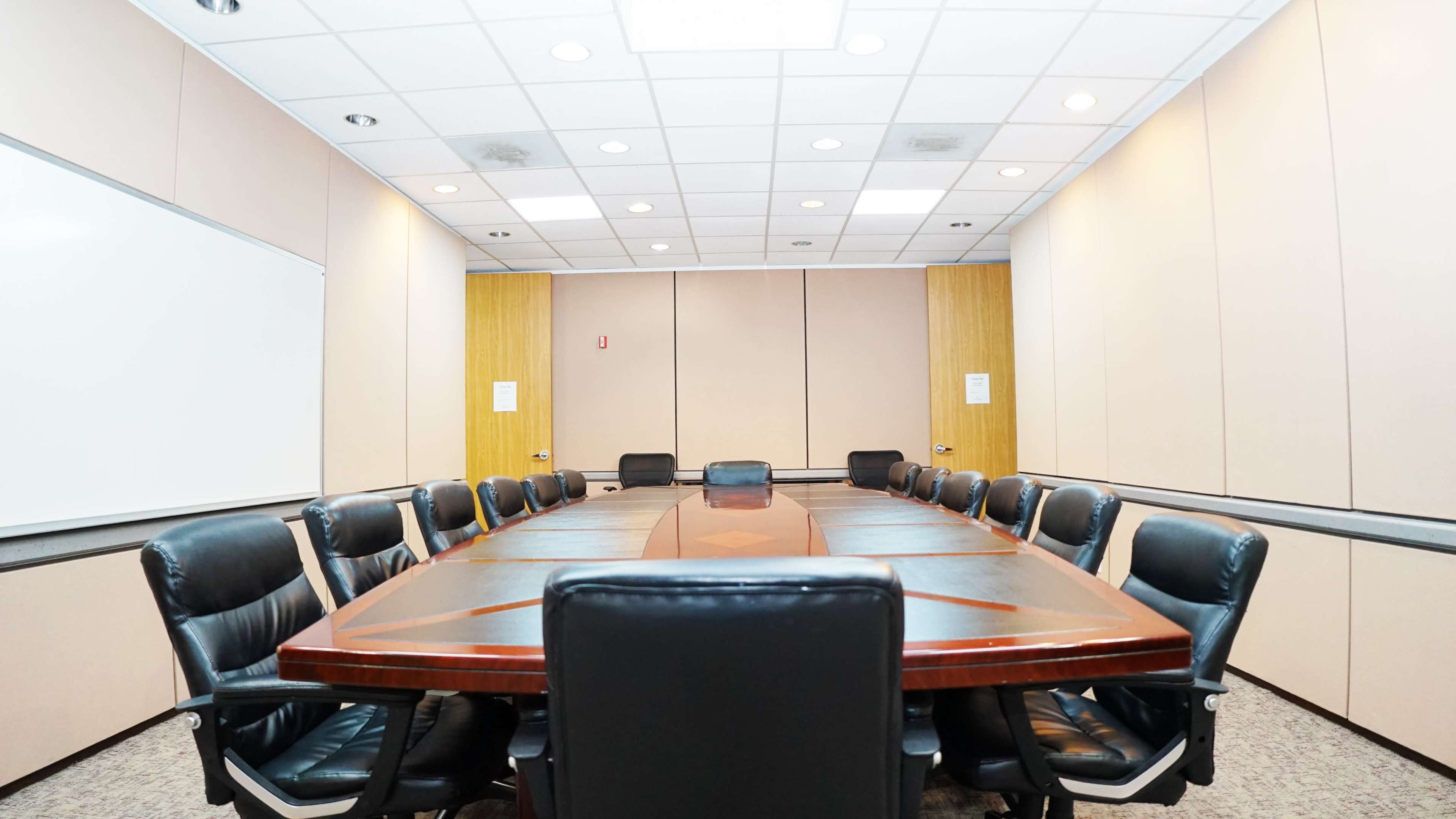 A formal conference room with a large wooden table surrounded by black leather chairs.