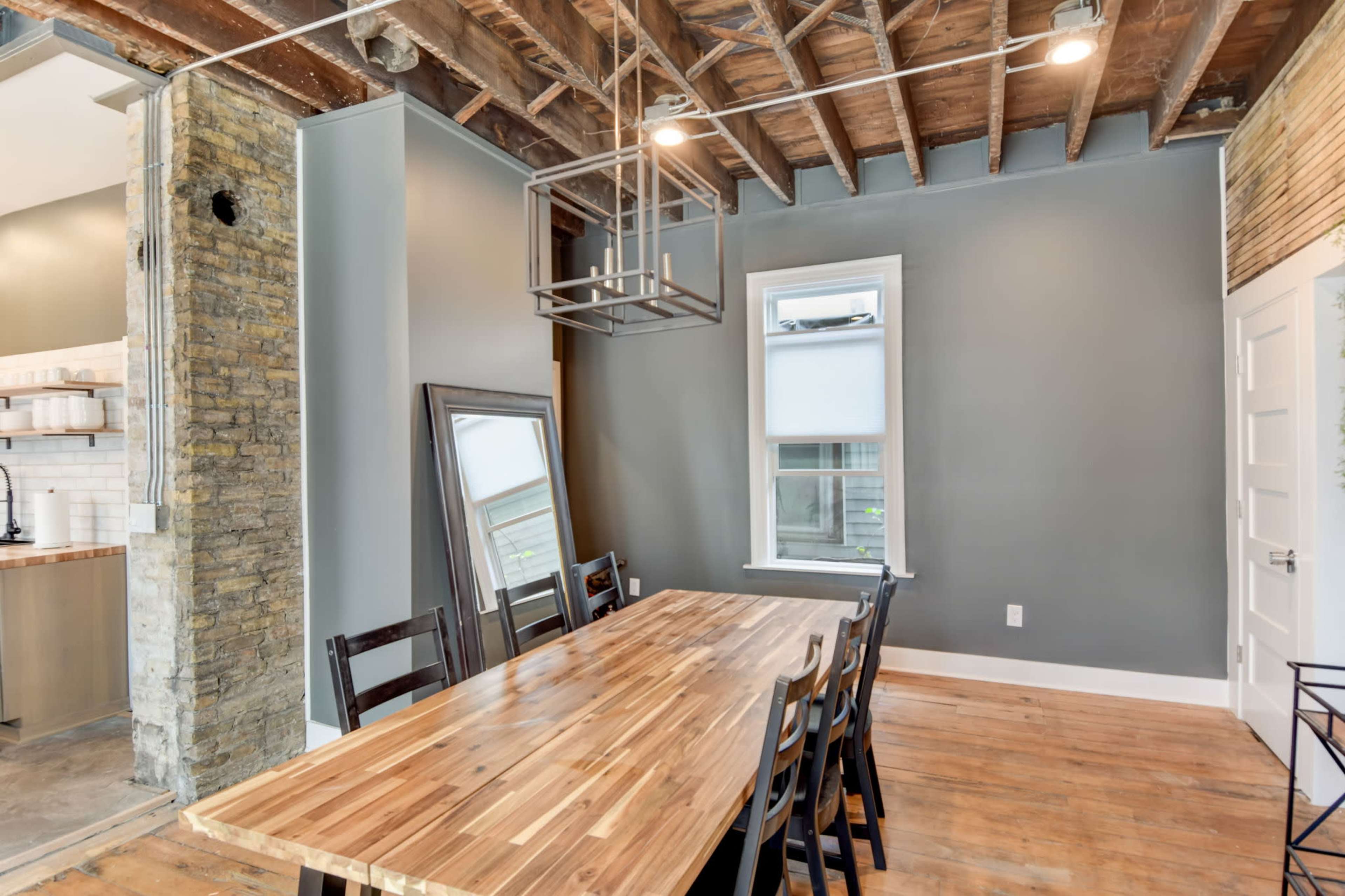 A spacious dining area features a wooden table surrounded by black chairs, with exposed beams and a large mirror against the wall.