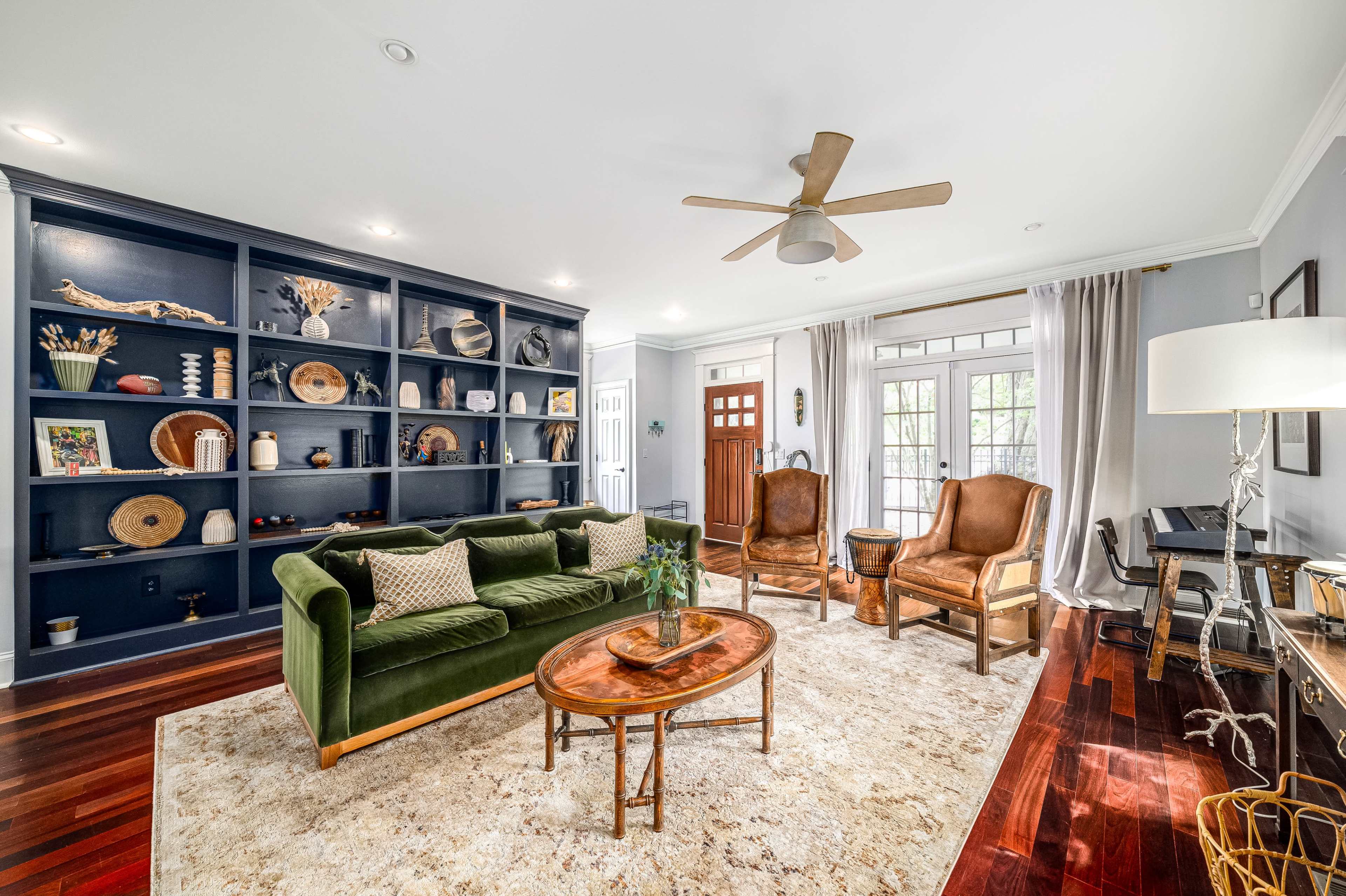 The living room features a green sofa, two brown armchairs, a wooden coffee table, and a large bookshelf filled with decorative items.