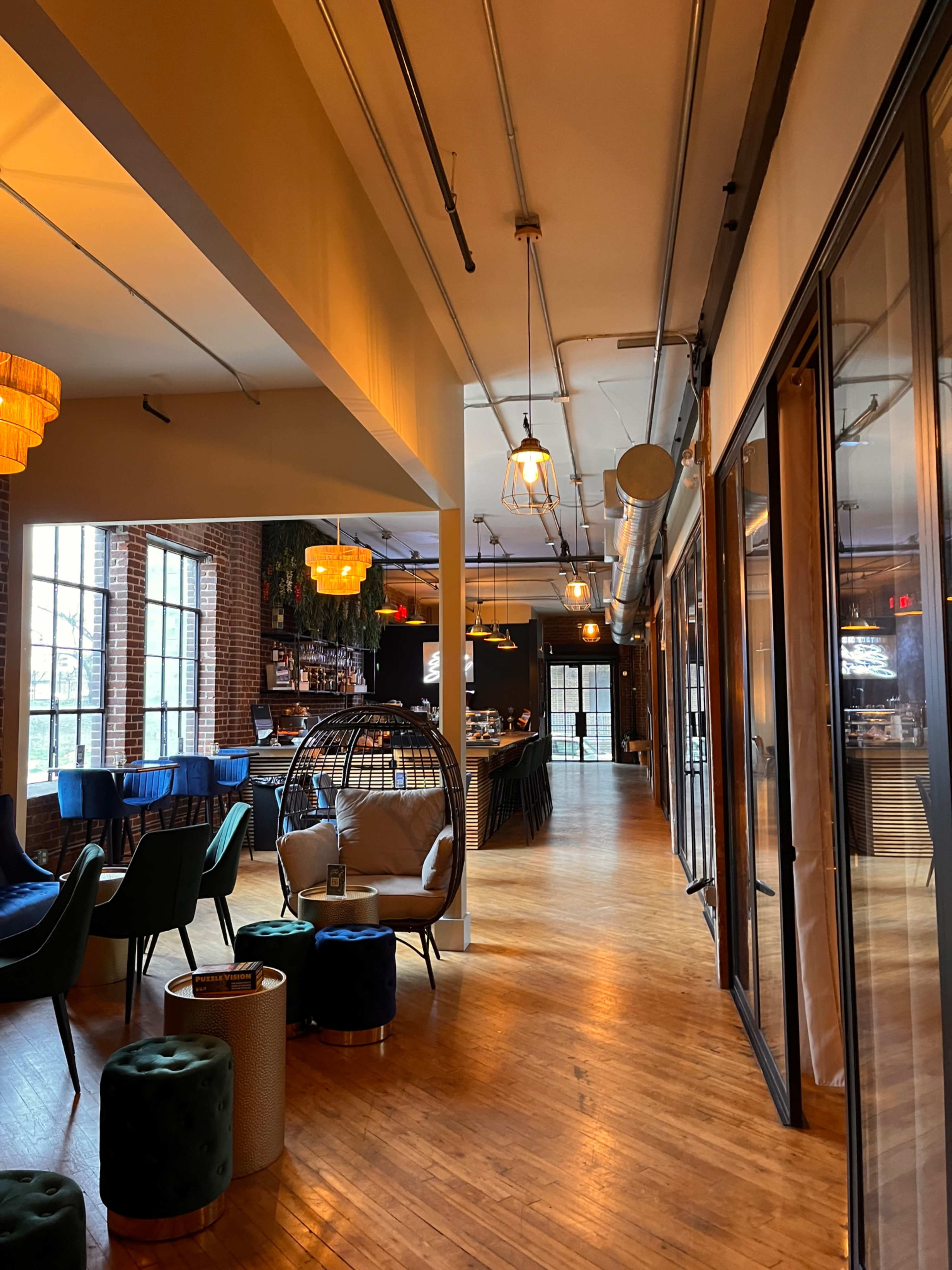 A modern interior of a spacious café or lounge with wooden floors, large windows, and various seating areas.