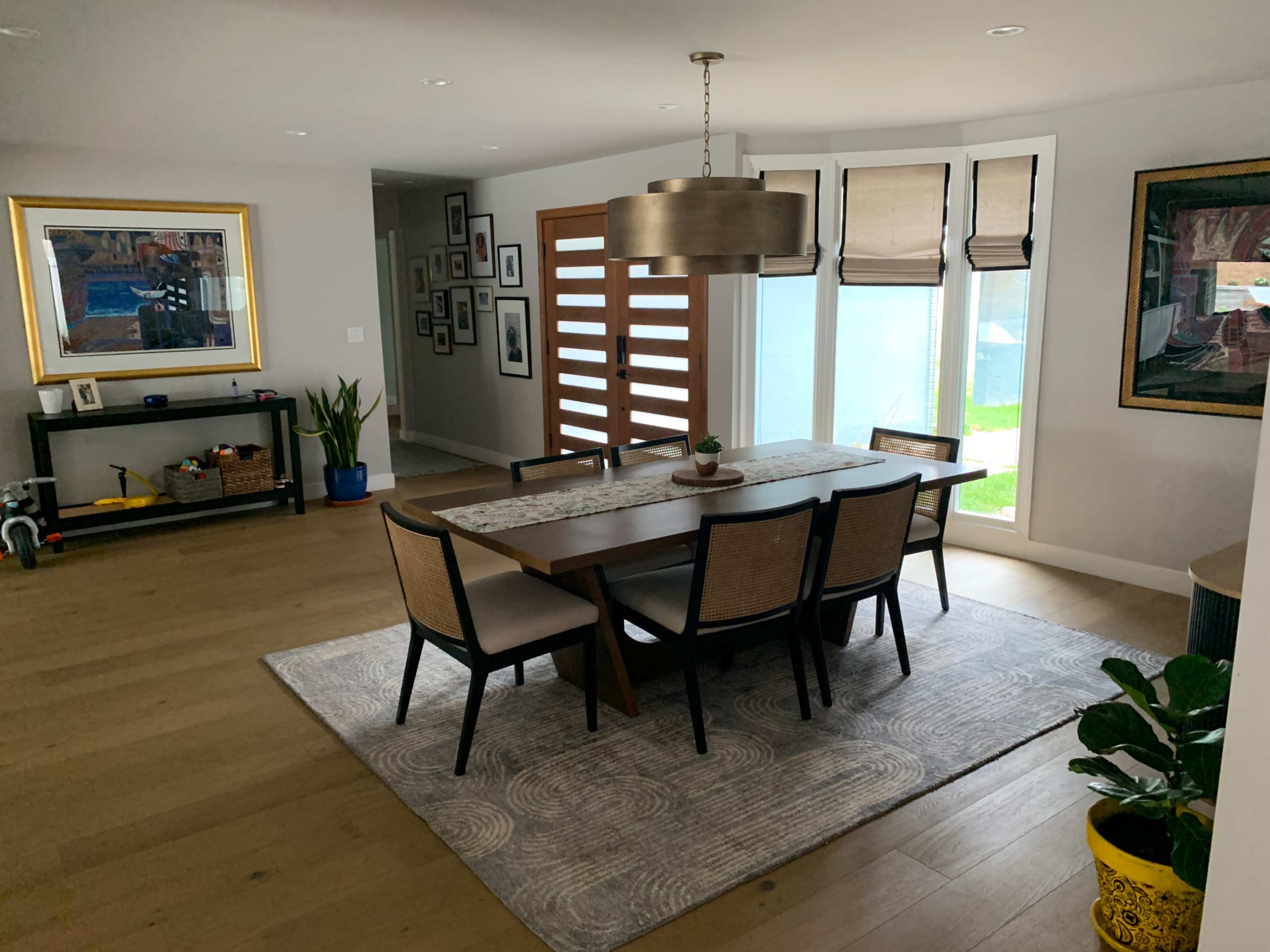 A modern dining room featuring a large wooden table surrounded by chairs, with large windows and artwork on the walls.