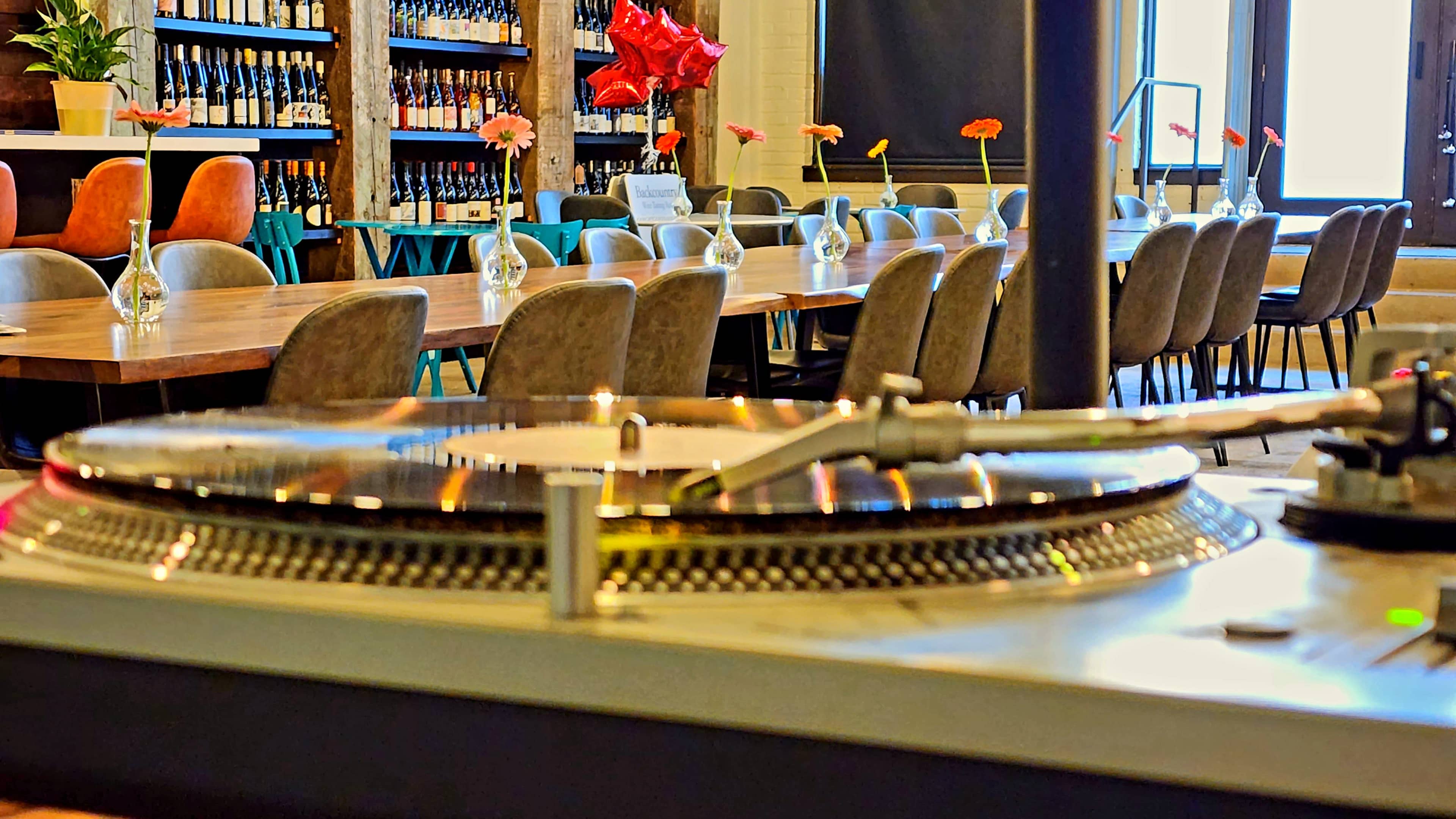 A close-up view of a turntable in the foreground, with a spacious restaurant setting featuring a long table and decorative flowers in vases in the background.