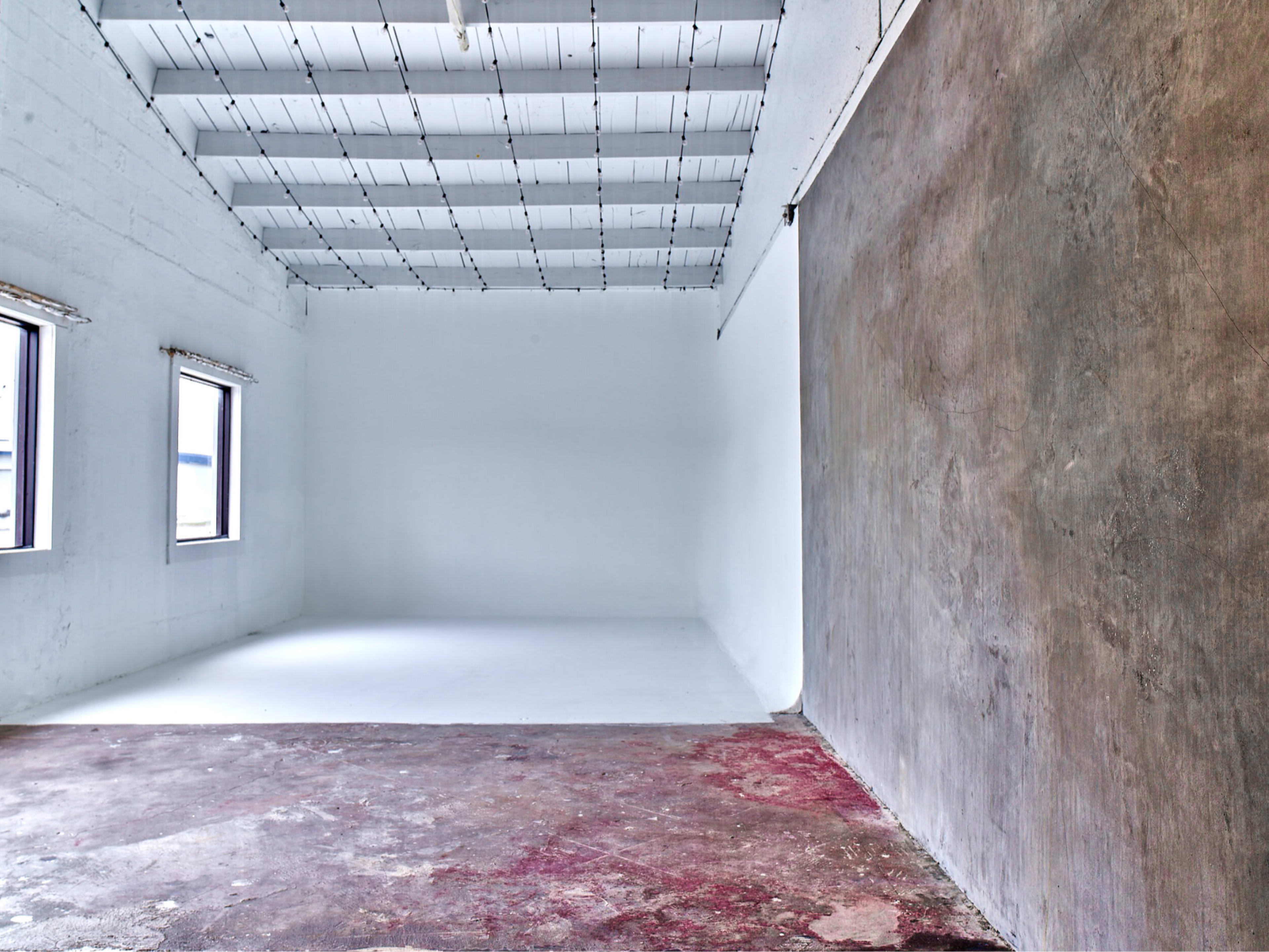 A spacious, empty room with a white ceiling, white walls, and a concrete wall on one side, featuring two windows.