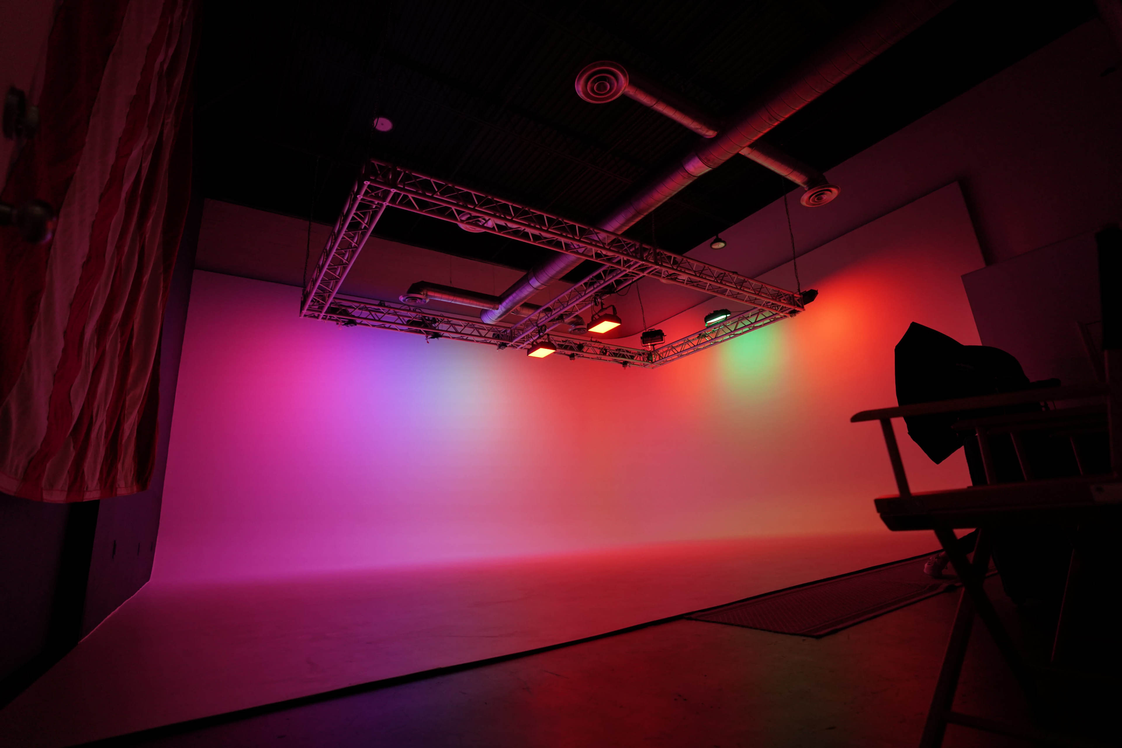The image shows a photography studio with a colorful gradient backdrop and a lighting rig suspended from the ceiling.