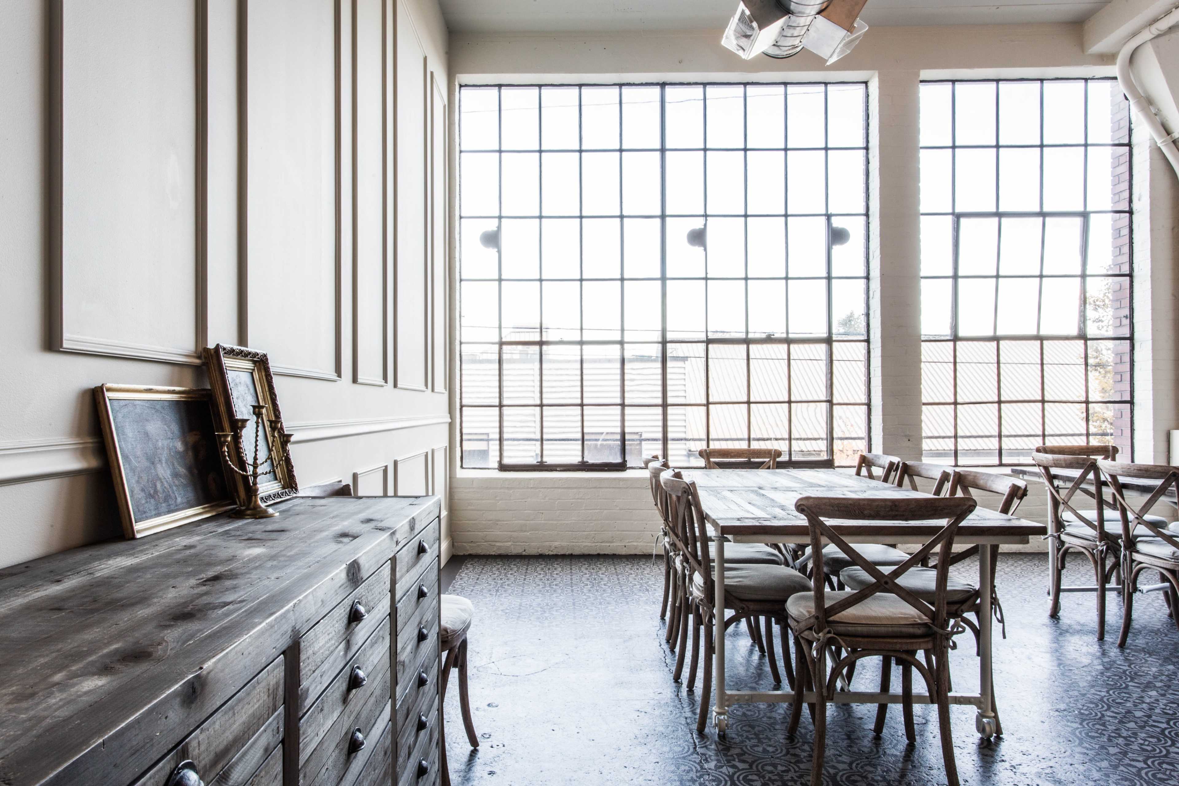 A spacious room with large windows, wooden furniture, and a long dining table accompanied by chairs.