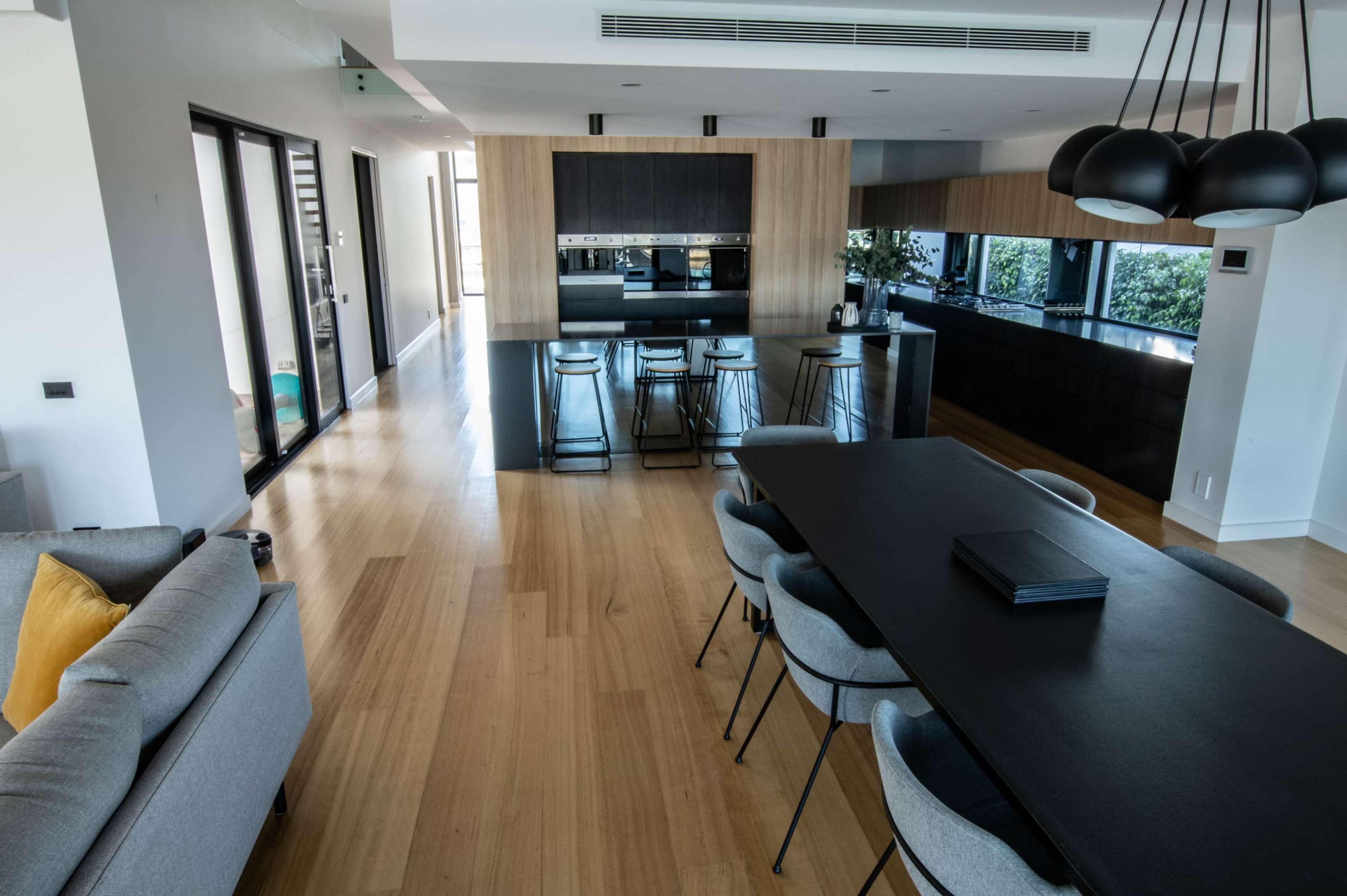 A modern open-concept kitchen and dining area with wooden flooring, a long dining table, and sleek black cabinetry.