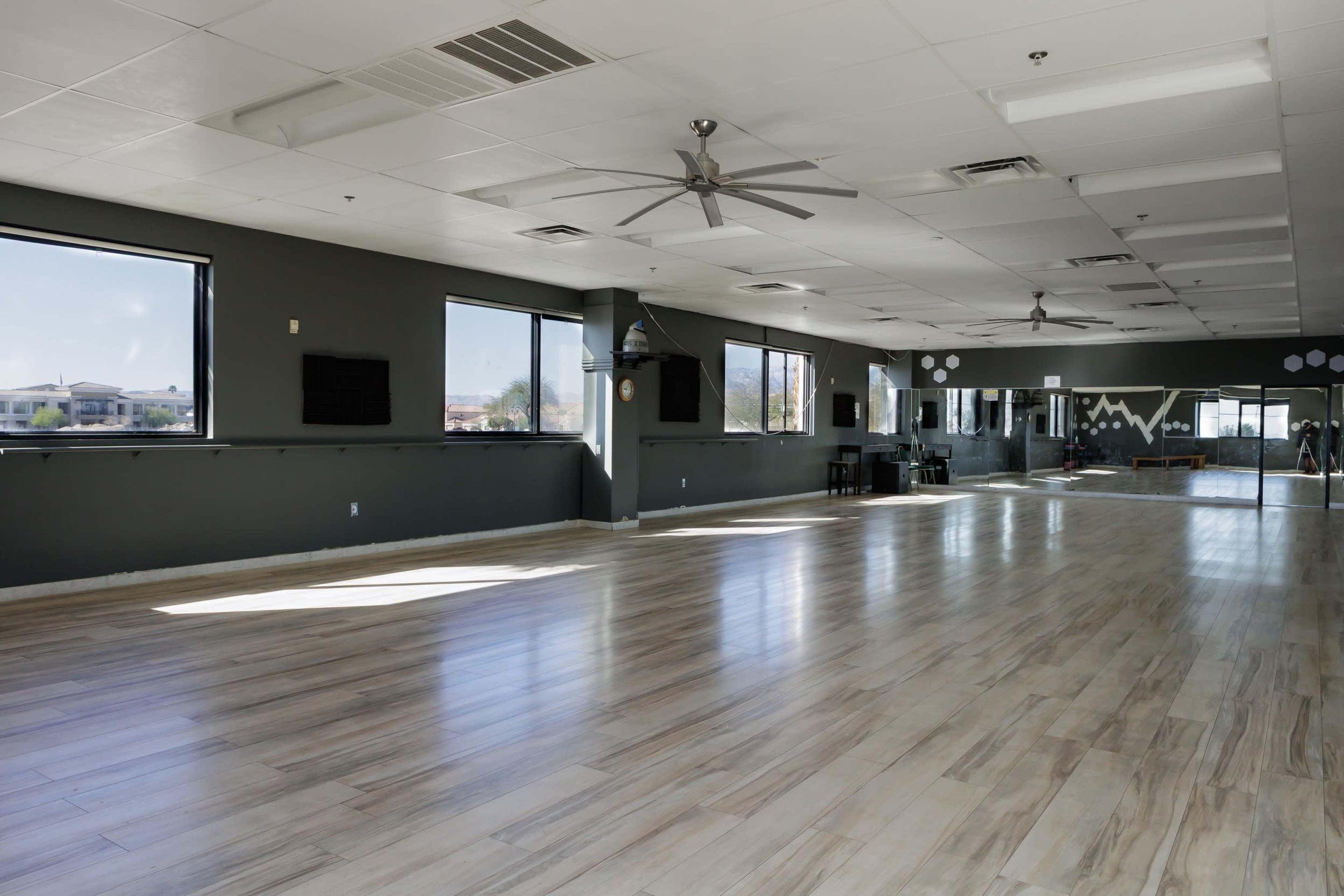 The image shows a spacious, well-lit dance studio with large windows and a polished wooden floor.