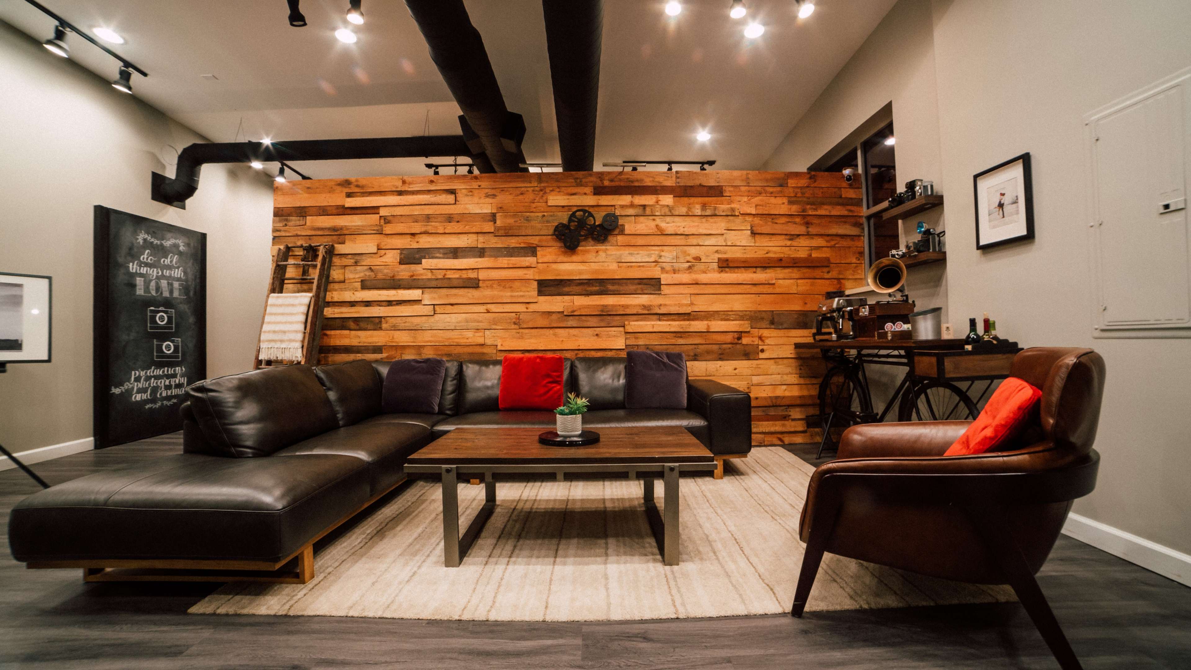 A modern living room with a large sectional sofa, a wooden accent wall, a coffee table, and a single armchair arranged on a light rug.