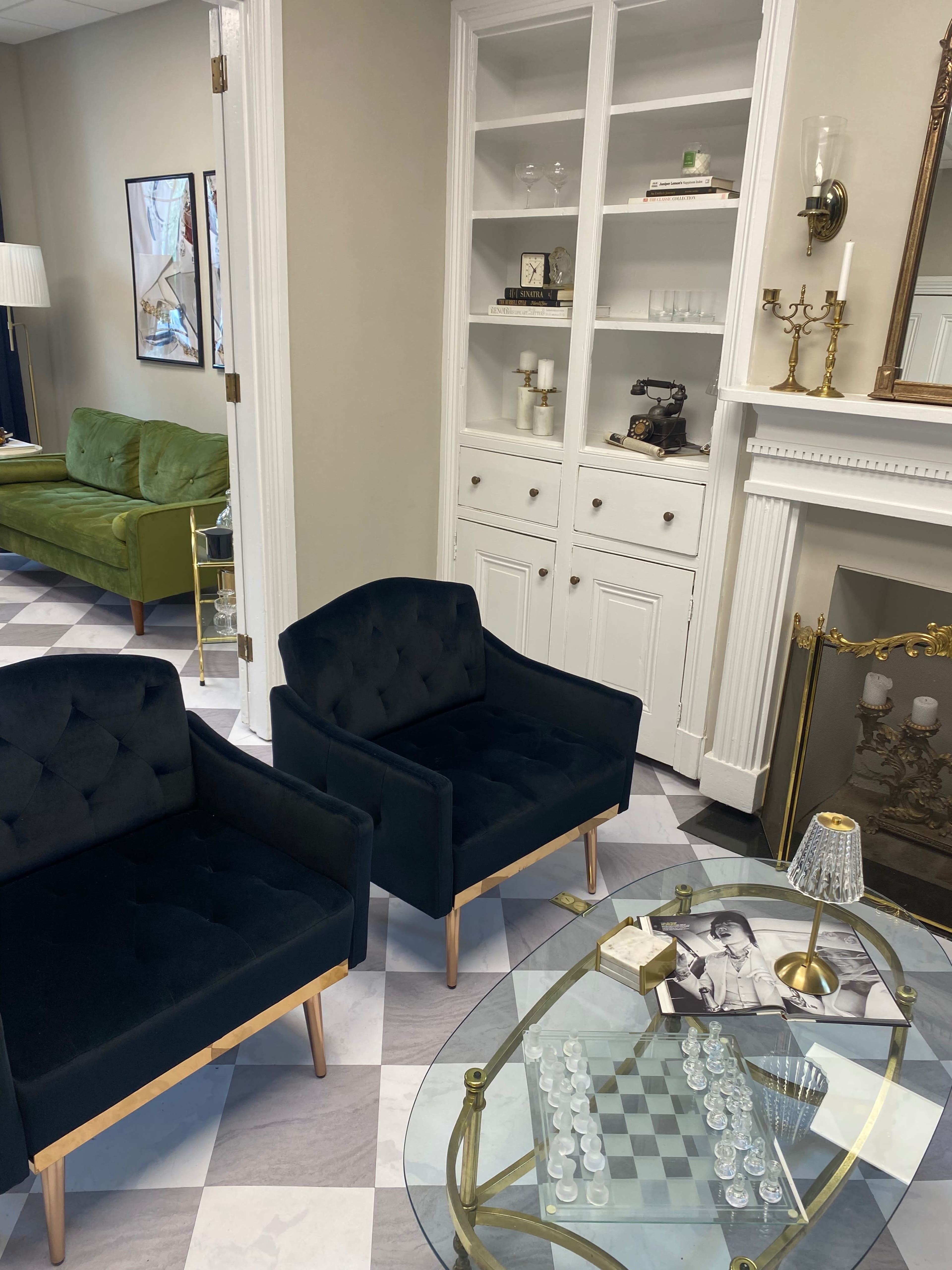The image shows a room with two black upholstered chairs, a glass chess table, and a white built-in cabinet against the wall.
