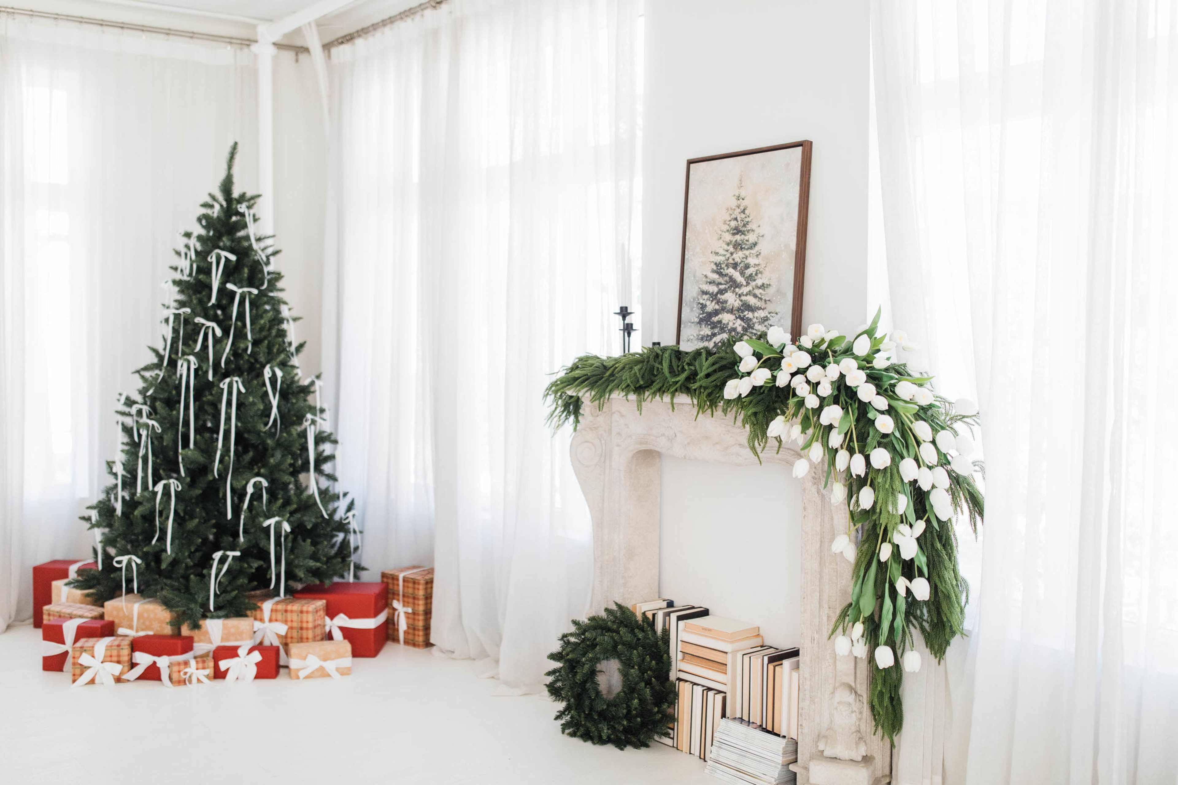 A decorated Christmas tree stands beside a fireplace adorned with greenery and white flowers, while gift-wrapped boxes are arranged at its base.