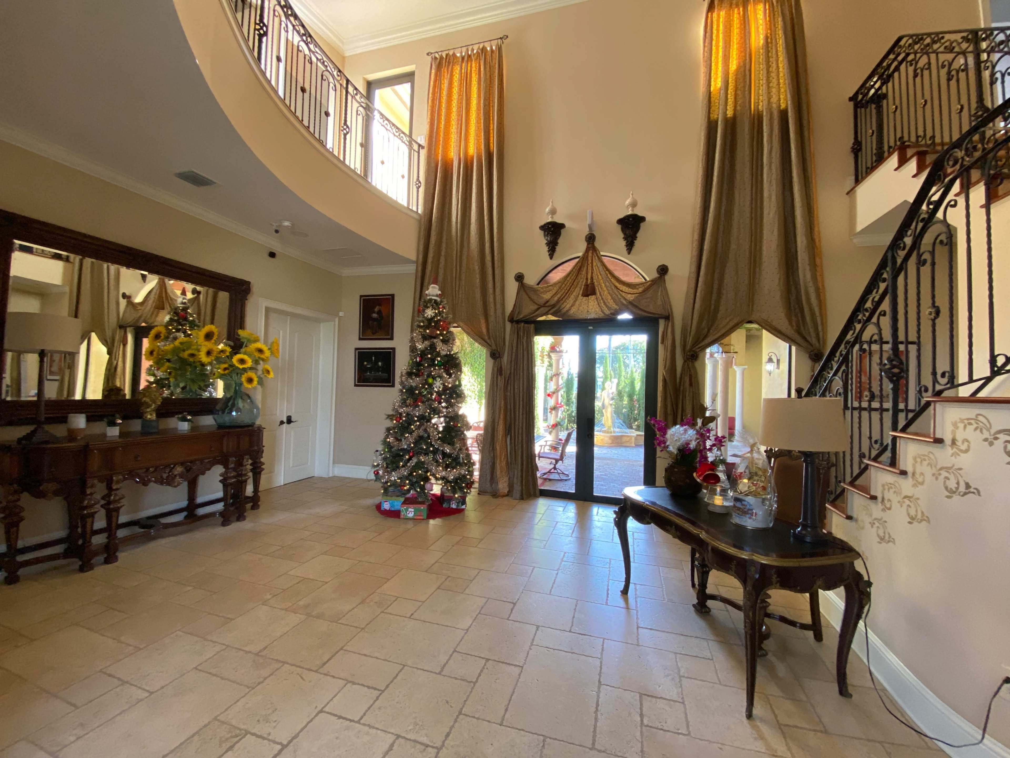 A spacious entryway with a staircase, a large mirror, a decorated Christmas tree, and a set of glass doors leading to an outdoor area.