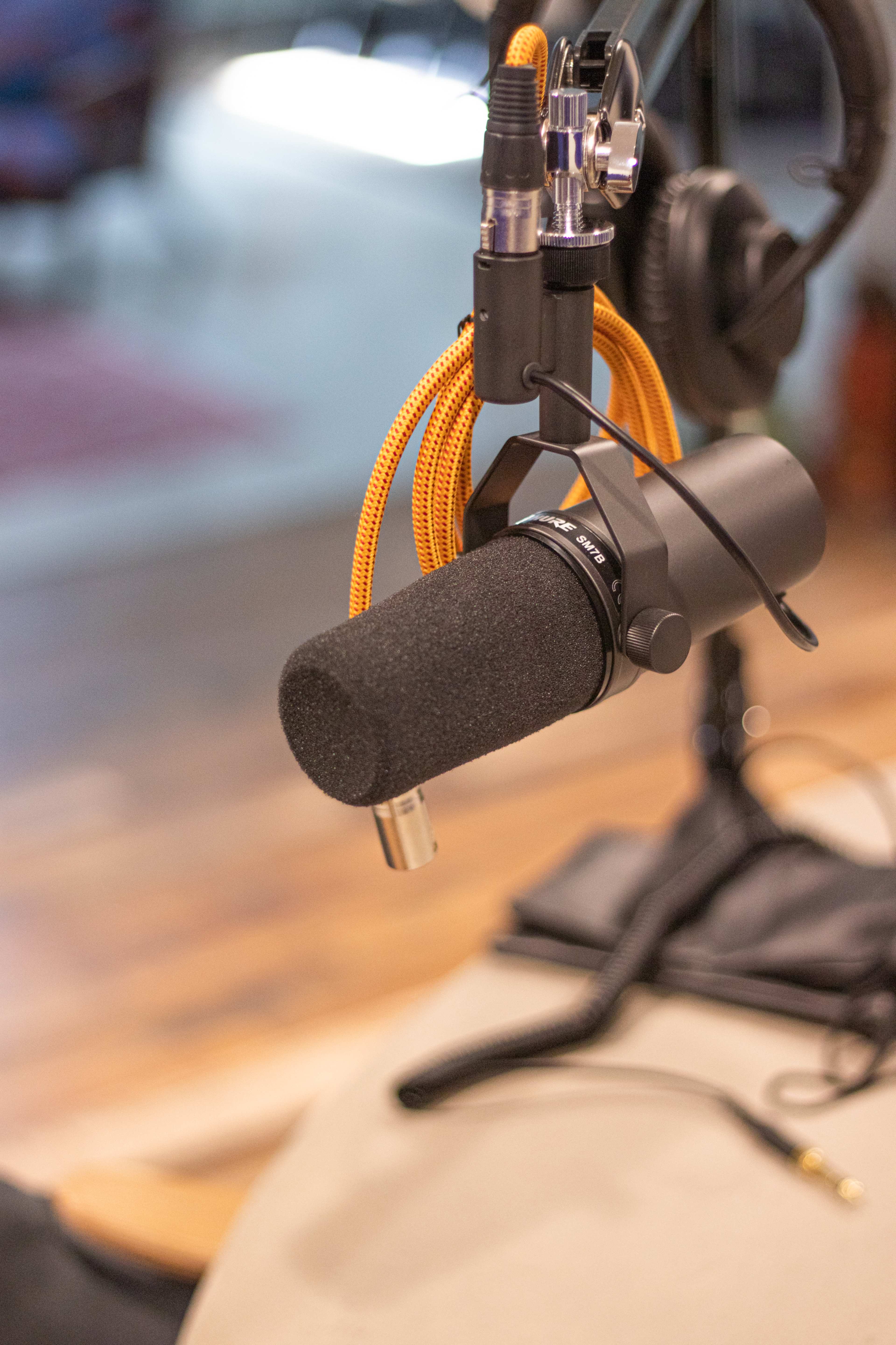 A black microphone with an orange cable hangs from a stand in a recording studio setting.