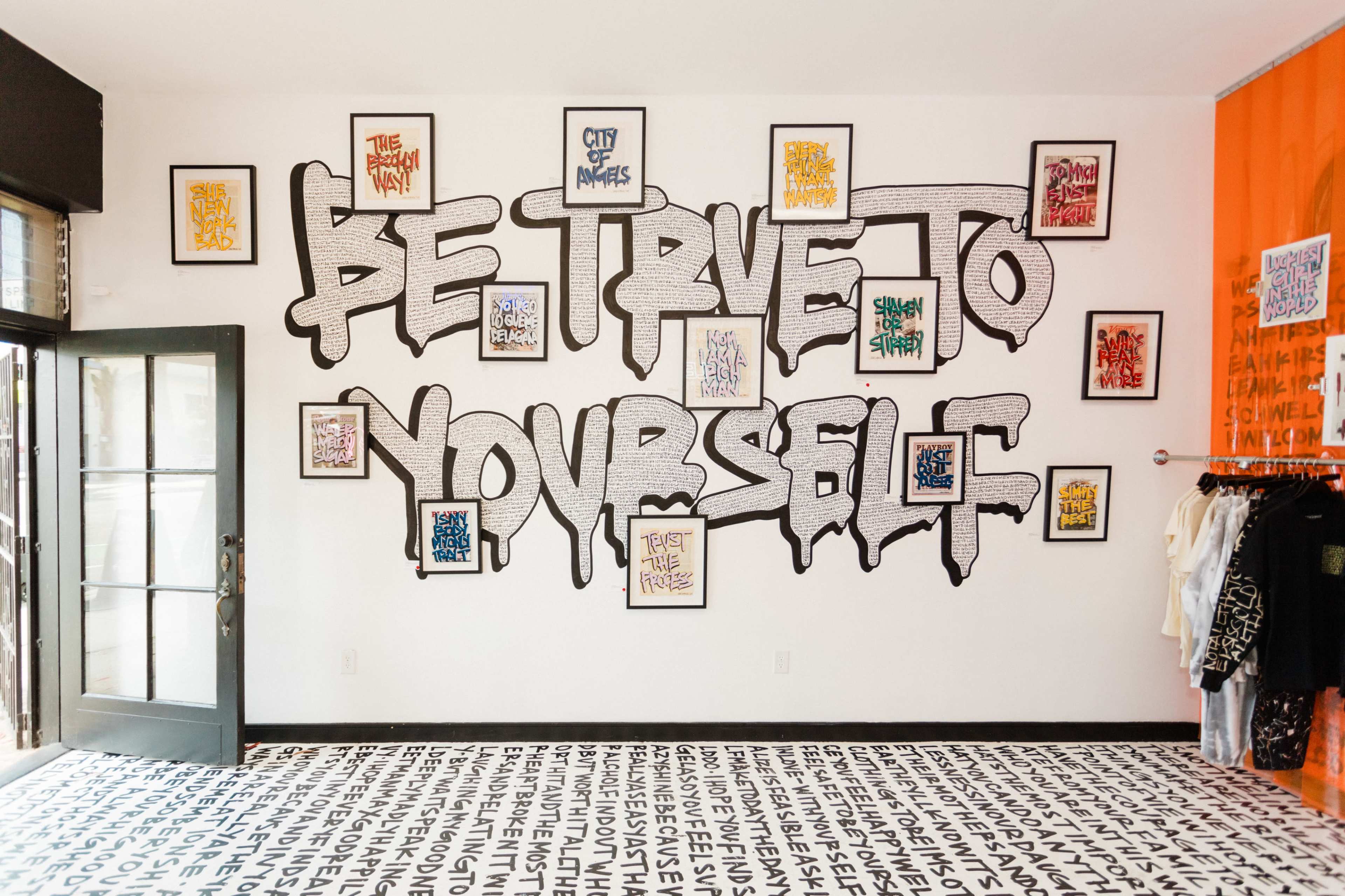 An art-filled room featuring a large mural that reads "BE TRUE TO YOURSELF" on the wall, surrounded by framed artworks and a patterned floor.
