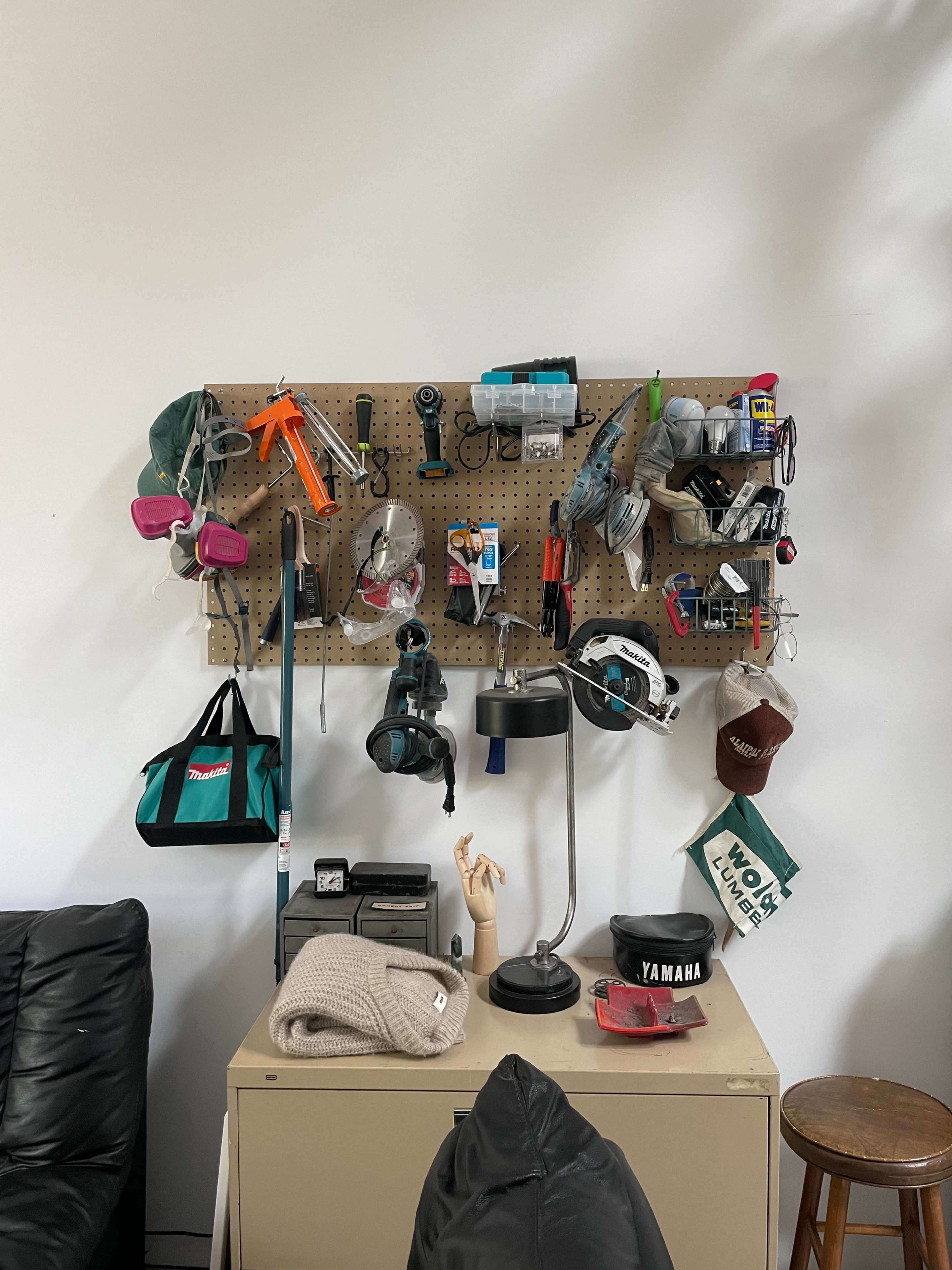 A pegboard wall displays various tools, equipment, and accessories, alongside a lamp and a chair in a room.