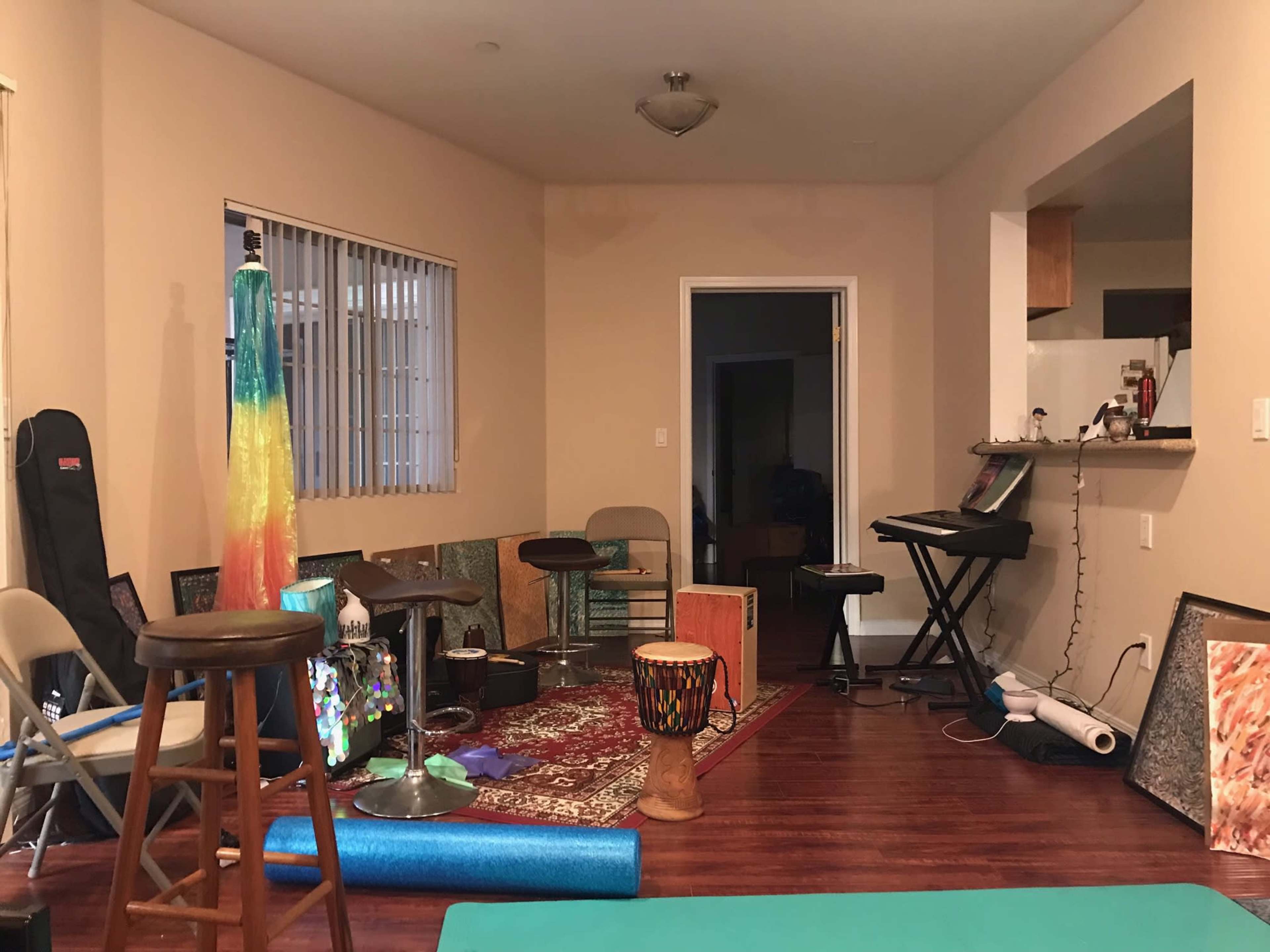 The room features a mix of furniture and musical instruments, with chairs and stools scattered around a patterned rug.