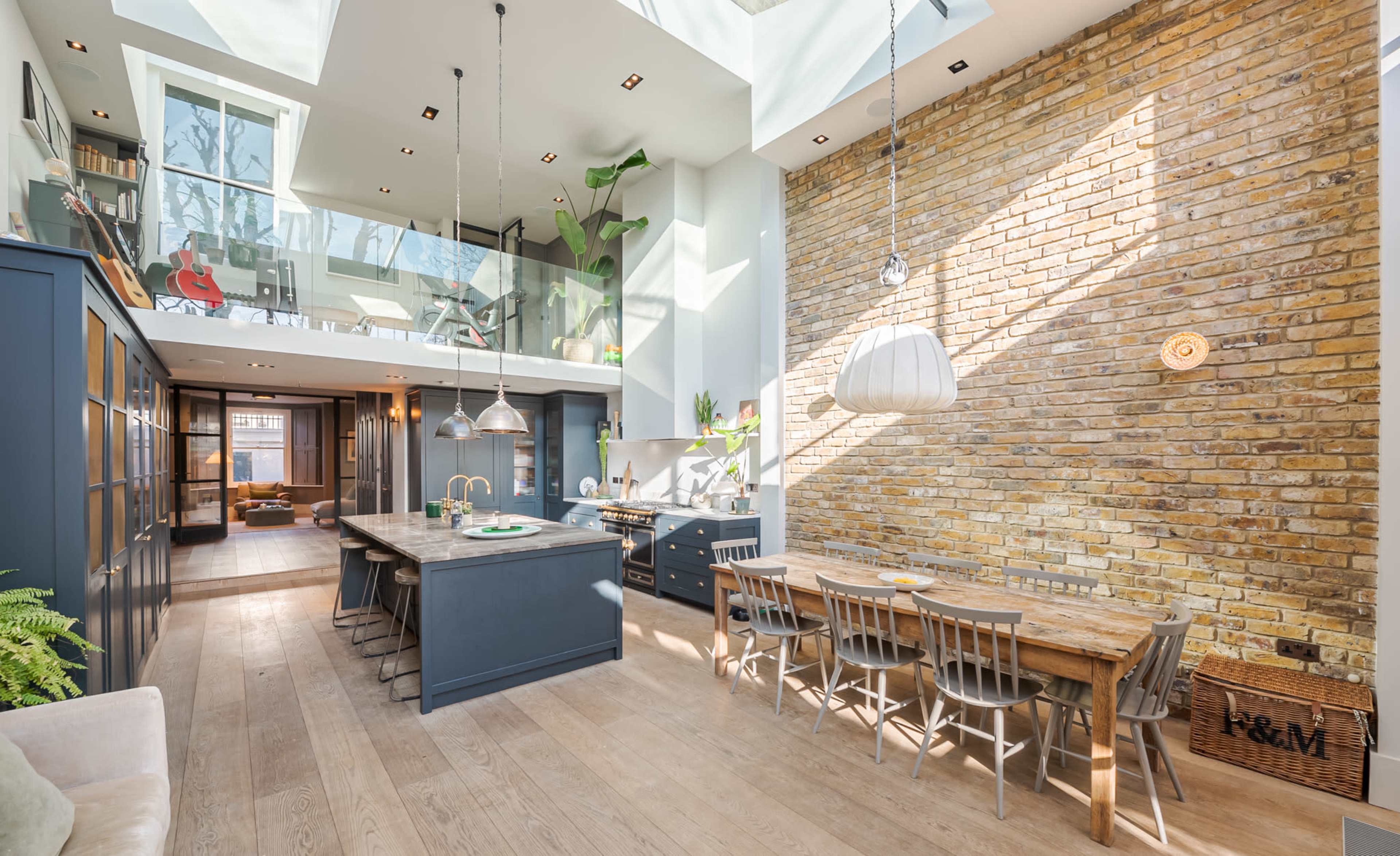 A modern kitchen and dining area with exposed brick walls, a large island, and ample natural light streaming through a skylight.