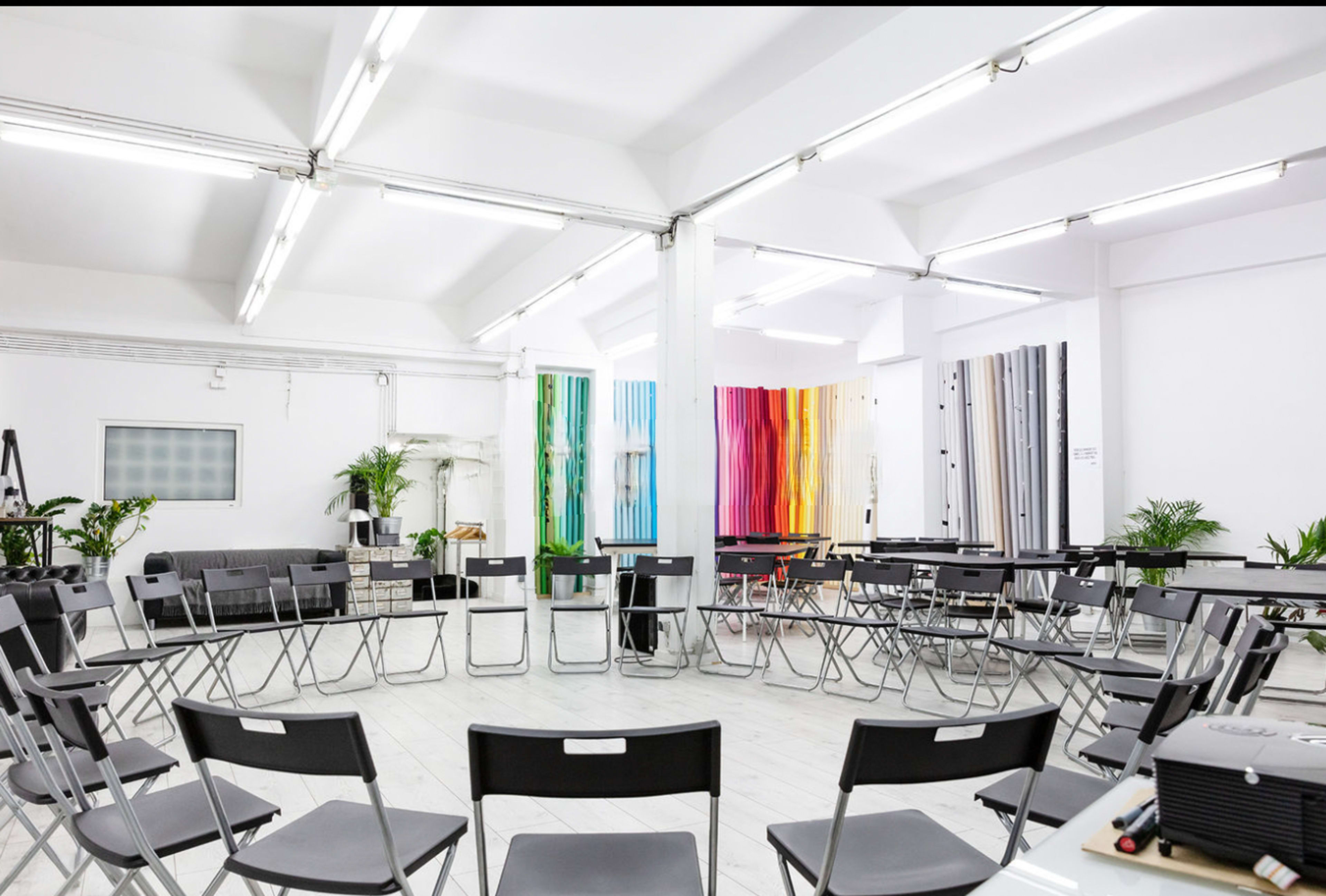 A spacious room with a circular arrangement of black folding chairs surrounding colorful vertical panels on the walls.