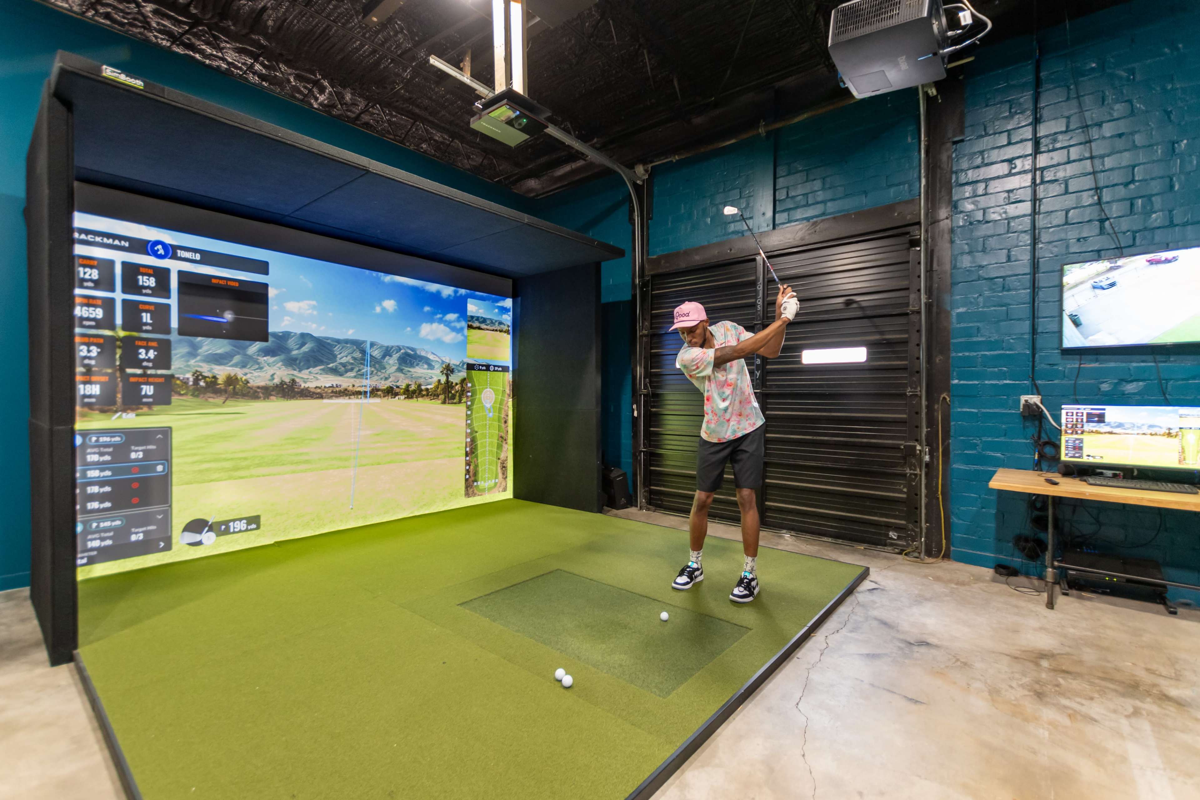 A person is swinging a golf club in a simulated golf environment with a large screen displaying a course and performance metrics.