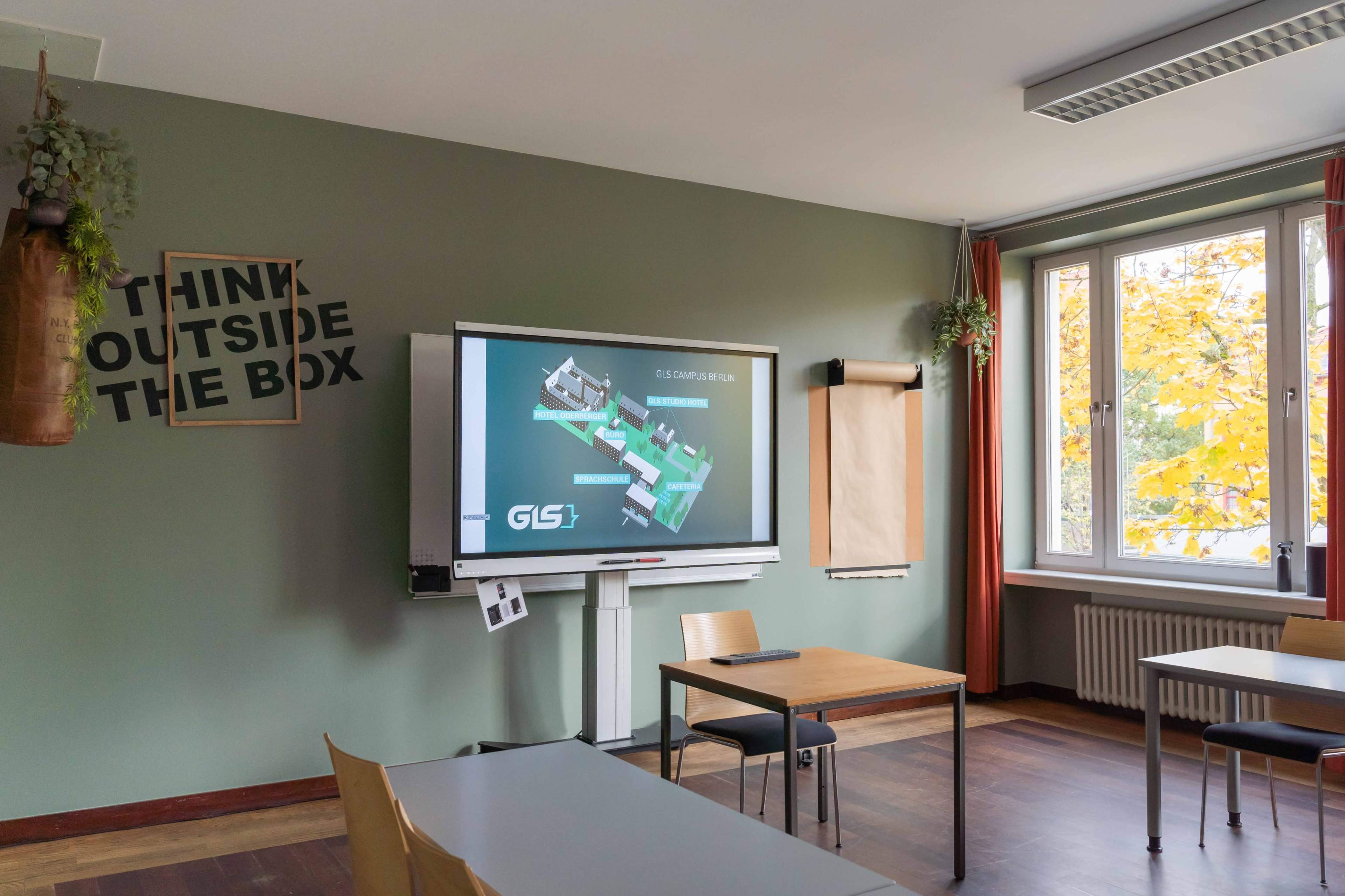 A classroom featuring a digital display showing a campus map, with a motivational poster on the wall and natural light coming through a window.