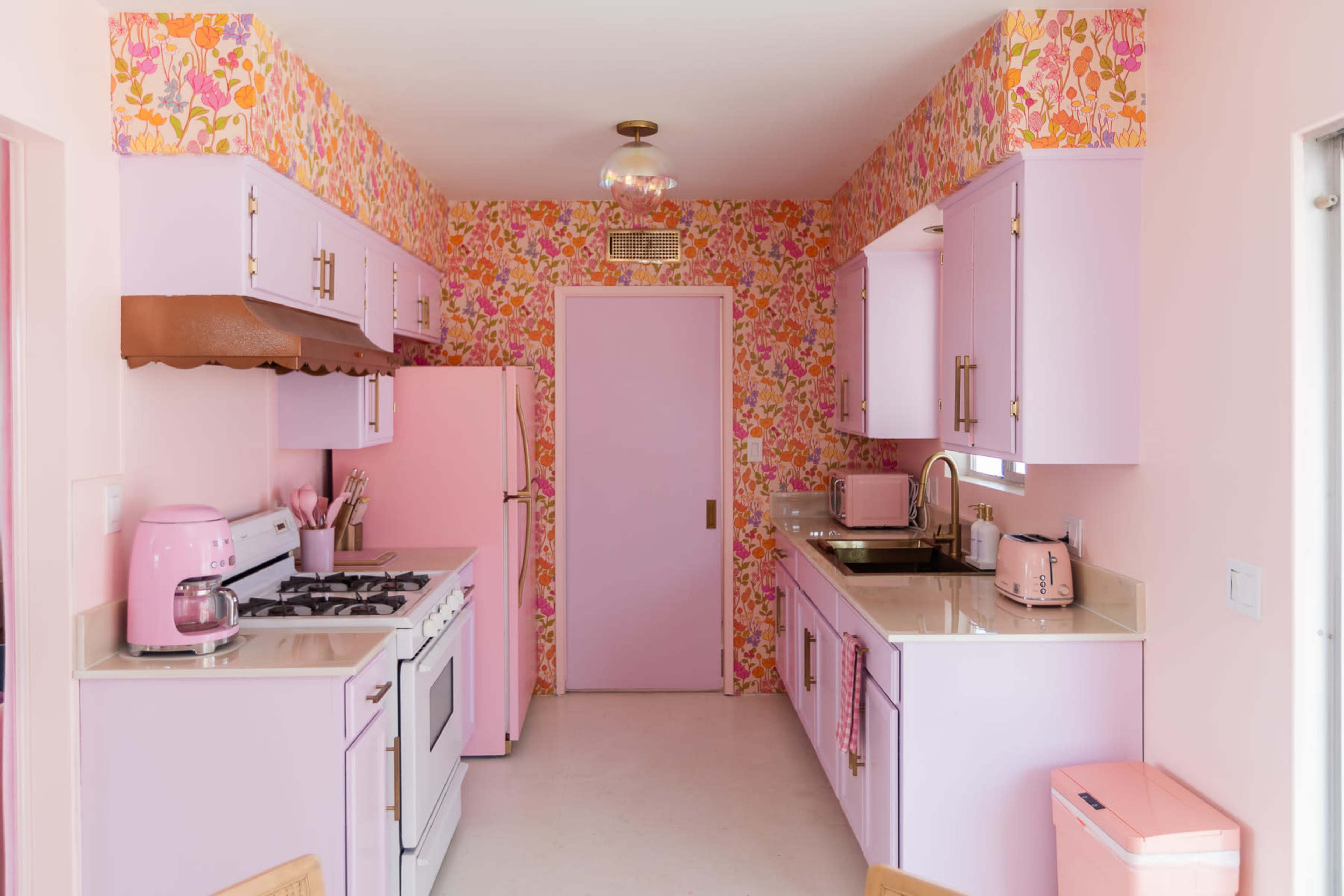 The kitchen features pastel pink and floral wallpaper, with lavender cabinets and appliances, including a pink refrigerator and toaster.