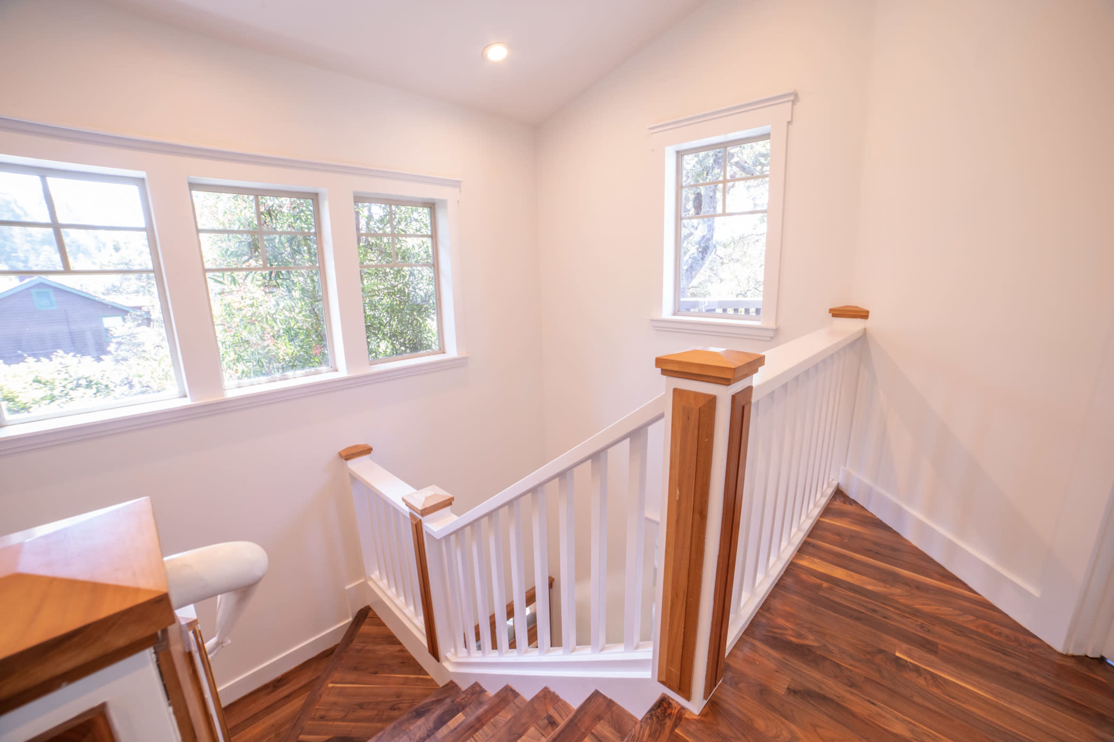 A brightly lit staircase leading to an upper level with white walls and large windows providing a view of greenery outside.