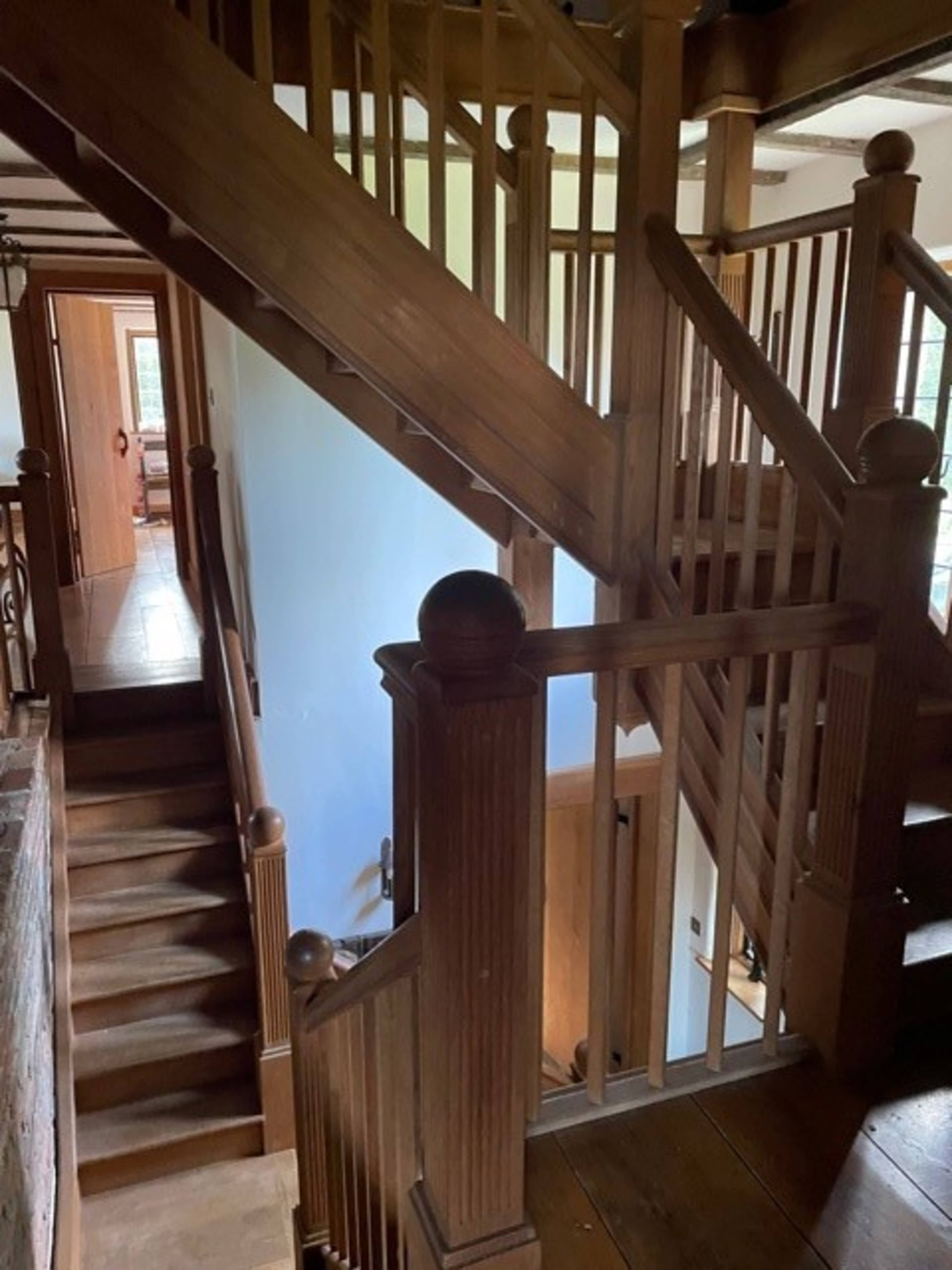 A wooden staircase with a balustrade, leading to an upper level in a well-lit interior space.