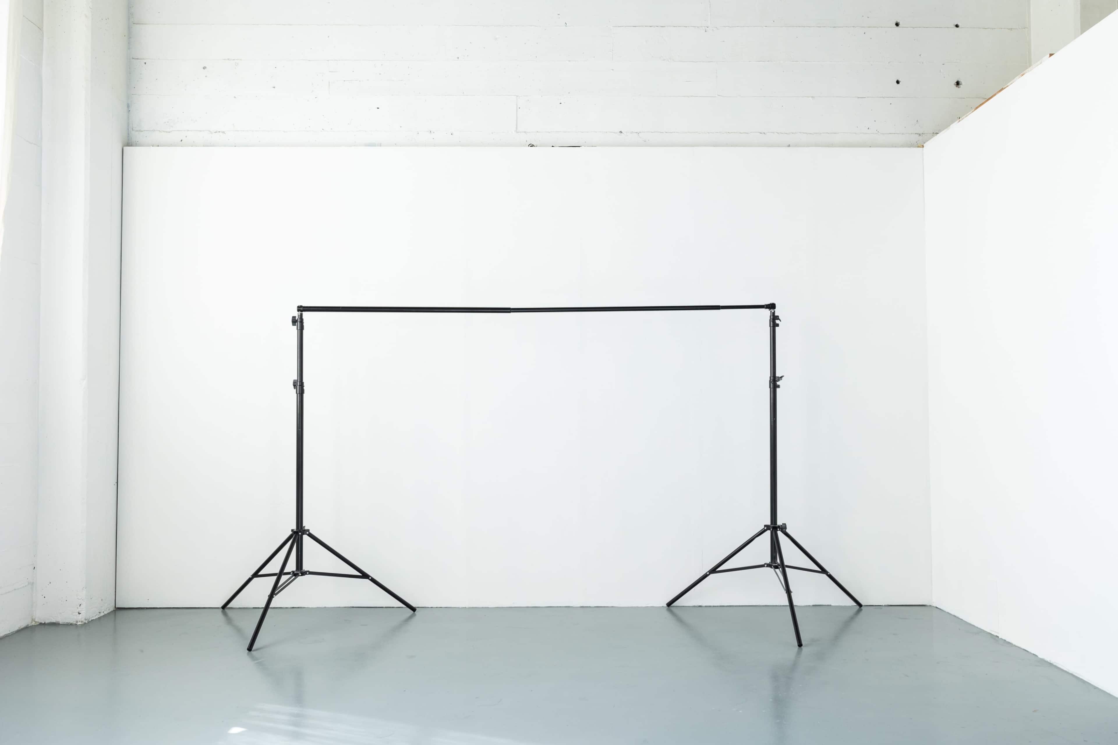 A black backdrop stand is positioned in front of a white wall in a minimalist room.
