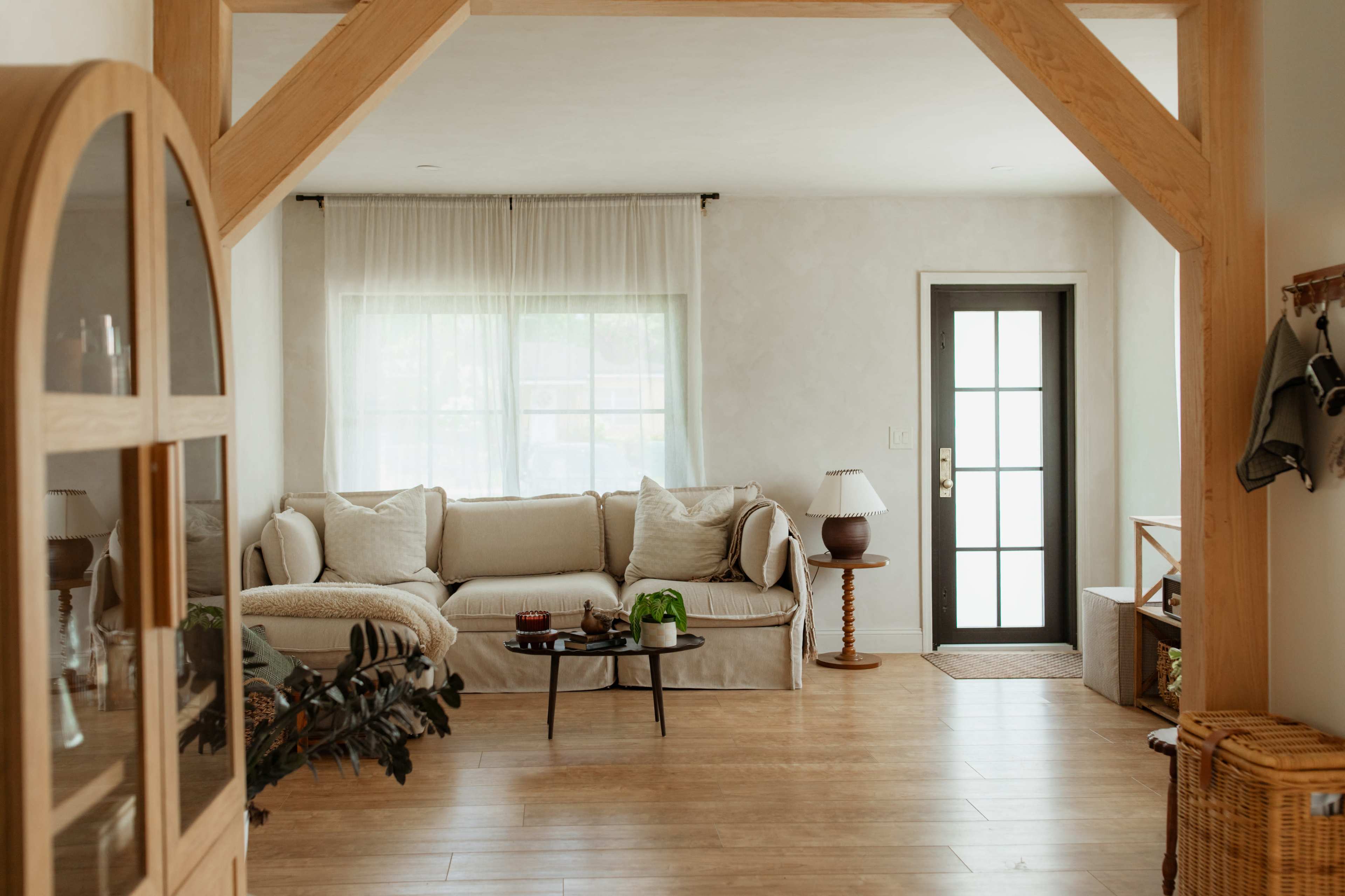 The image shows a cozy living room with a beige sofa, a coffee table, and a front door featuring glass panels, all set in a light and airy environment.