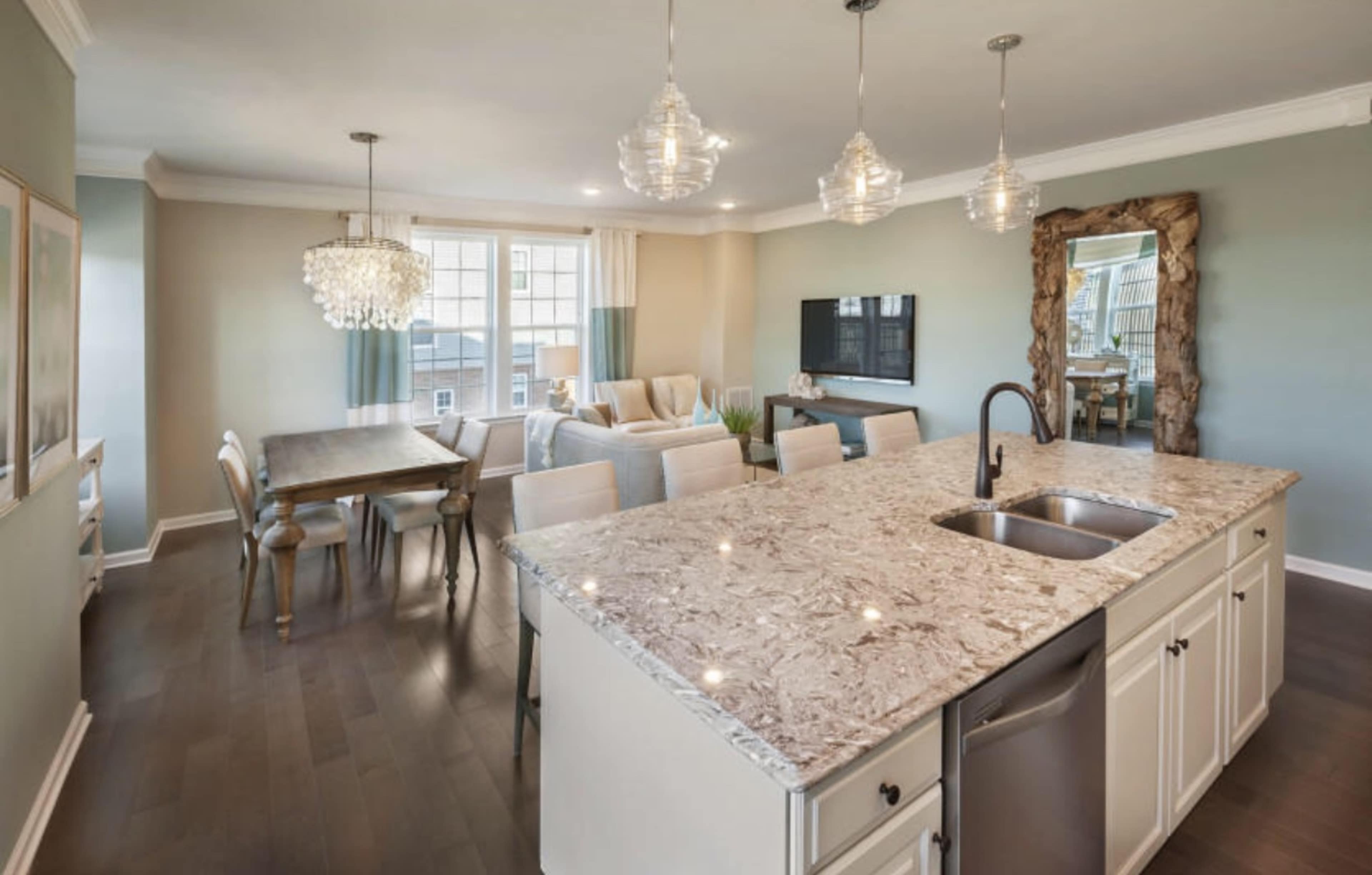 A modern open-concept living and dining area featuring a kitchen island with a sink, a dining table, a seating arrangement, and large windows.