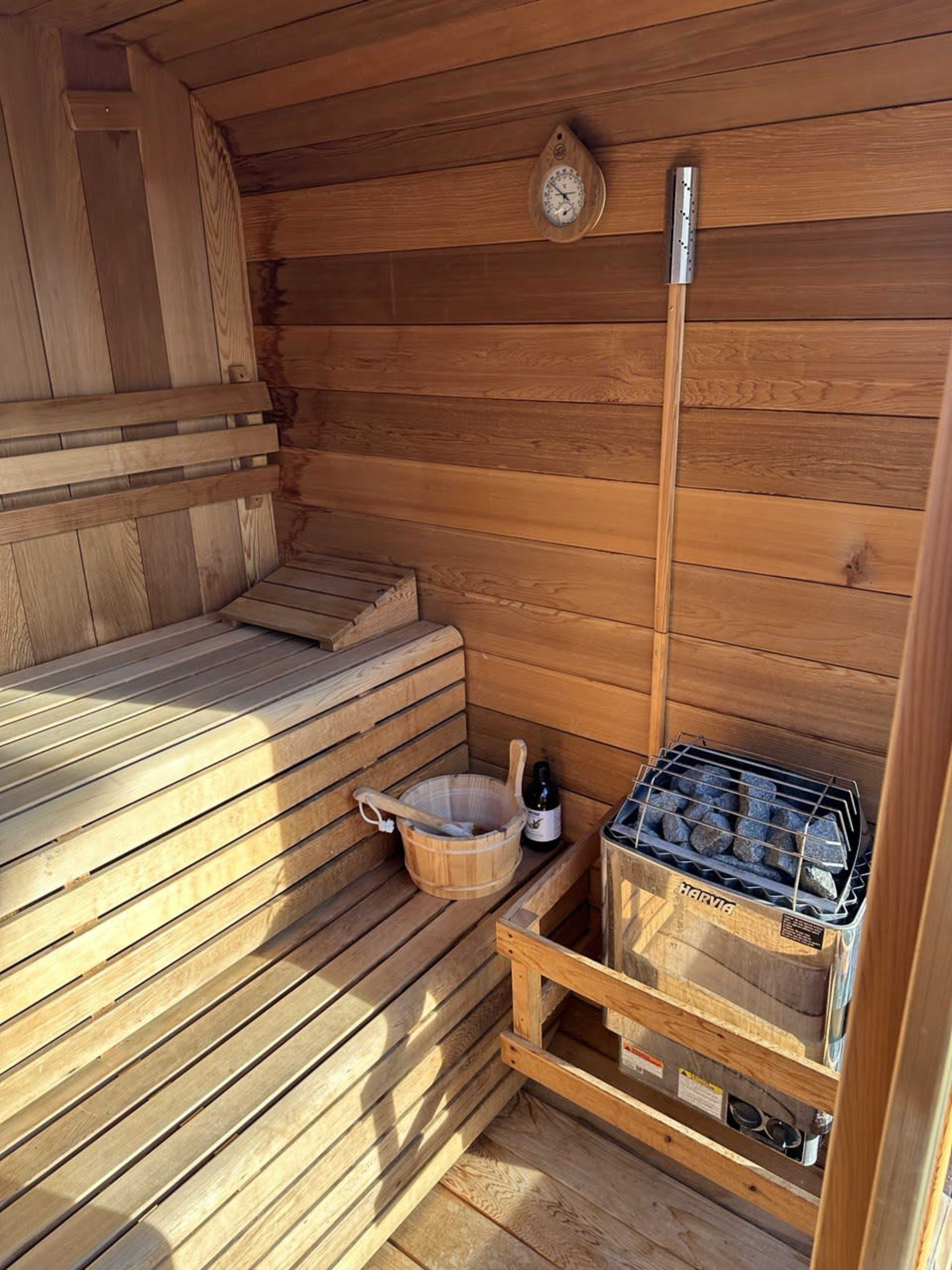 The interior of a wooden sauna with benches, a bucket, a ladle, and a stove filled with stones.