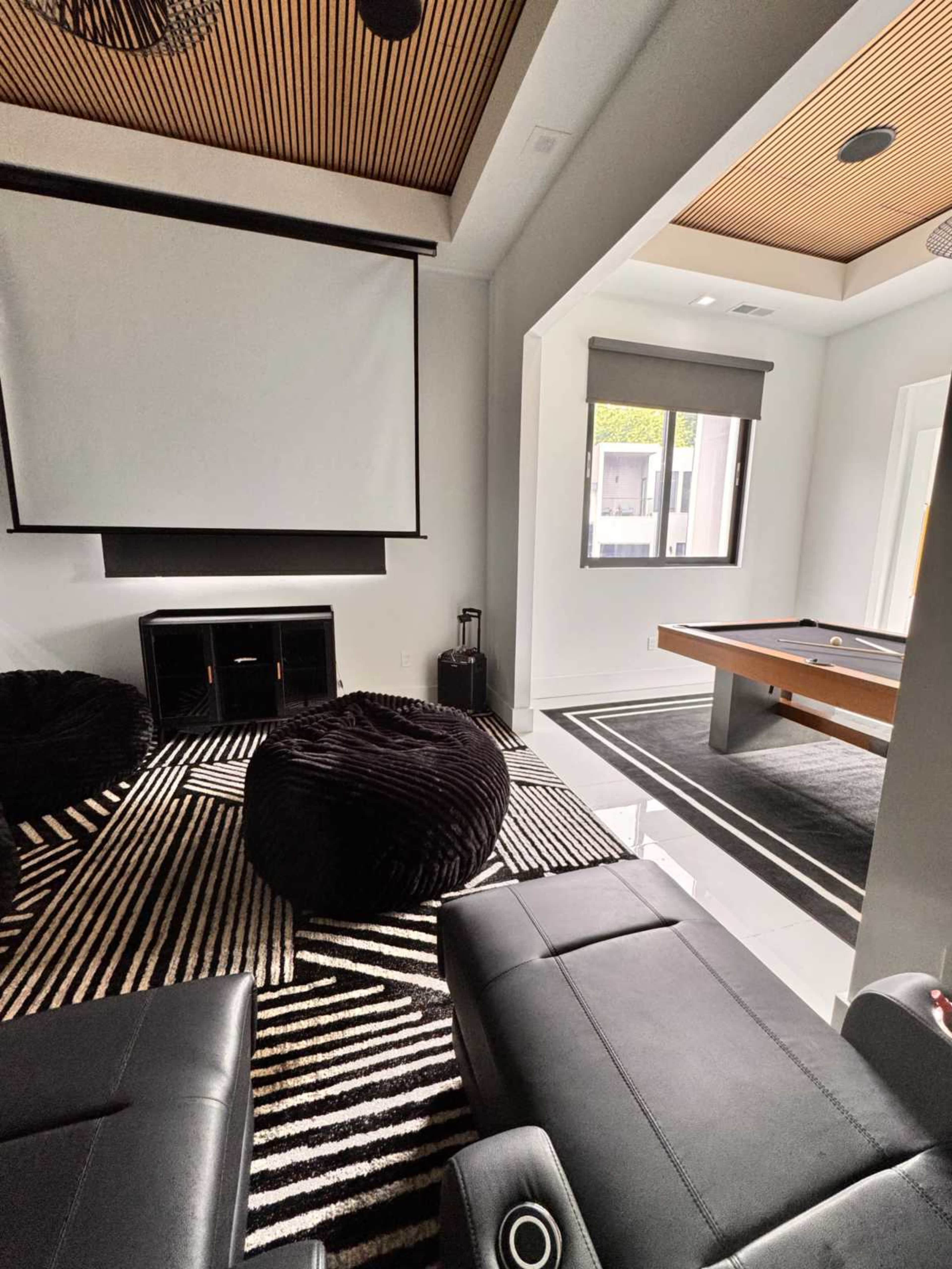 The image shows a modern room featuring a large projector screen, a pool table, and black bean bag chairs arranged on a striped rug.