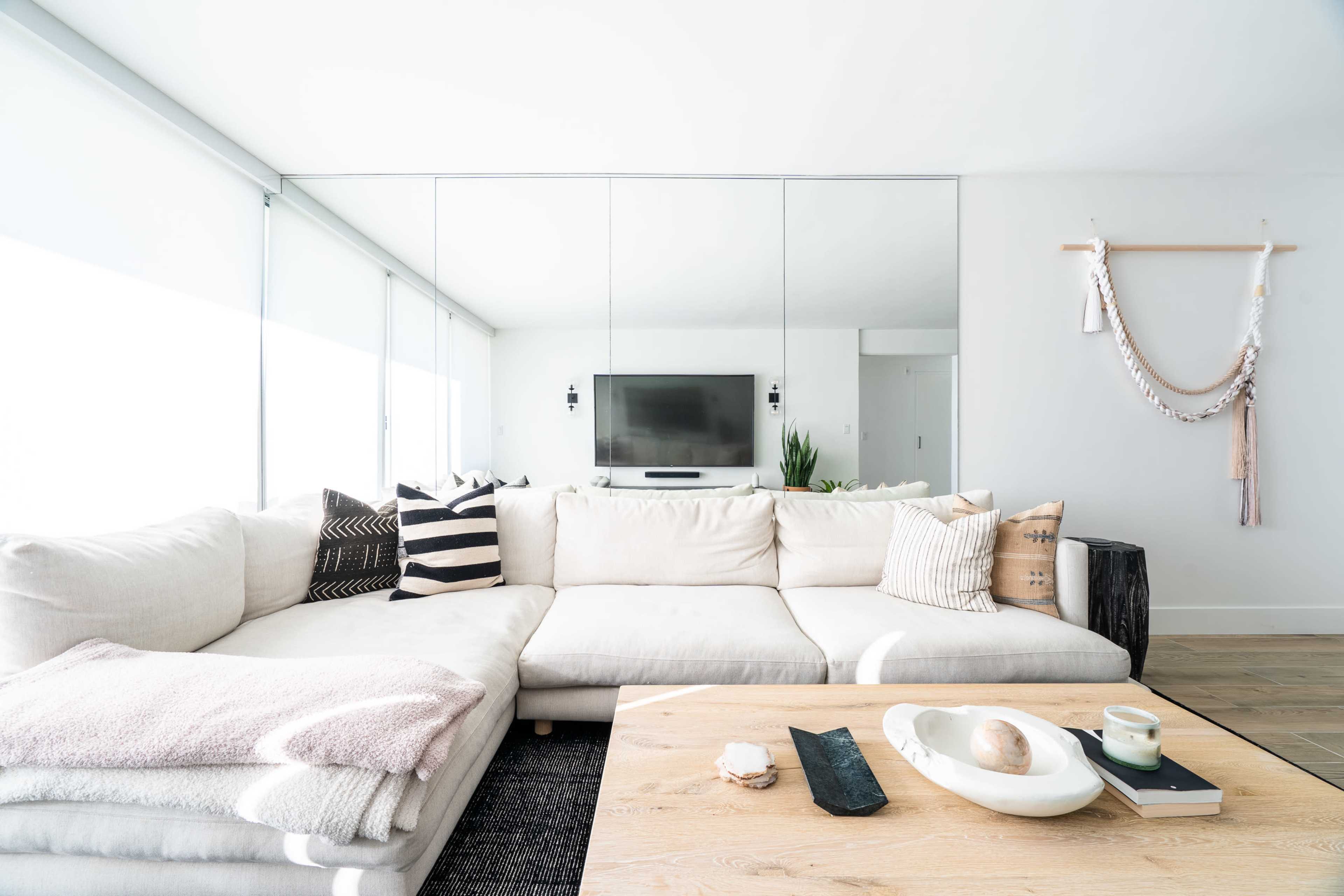 A modern living room with a large white sectional sofa, a wooden coffee table, and a wall-mounted television reflected in a mirror.