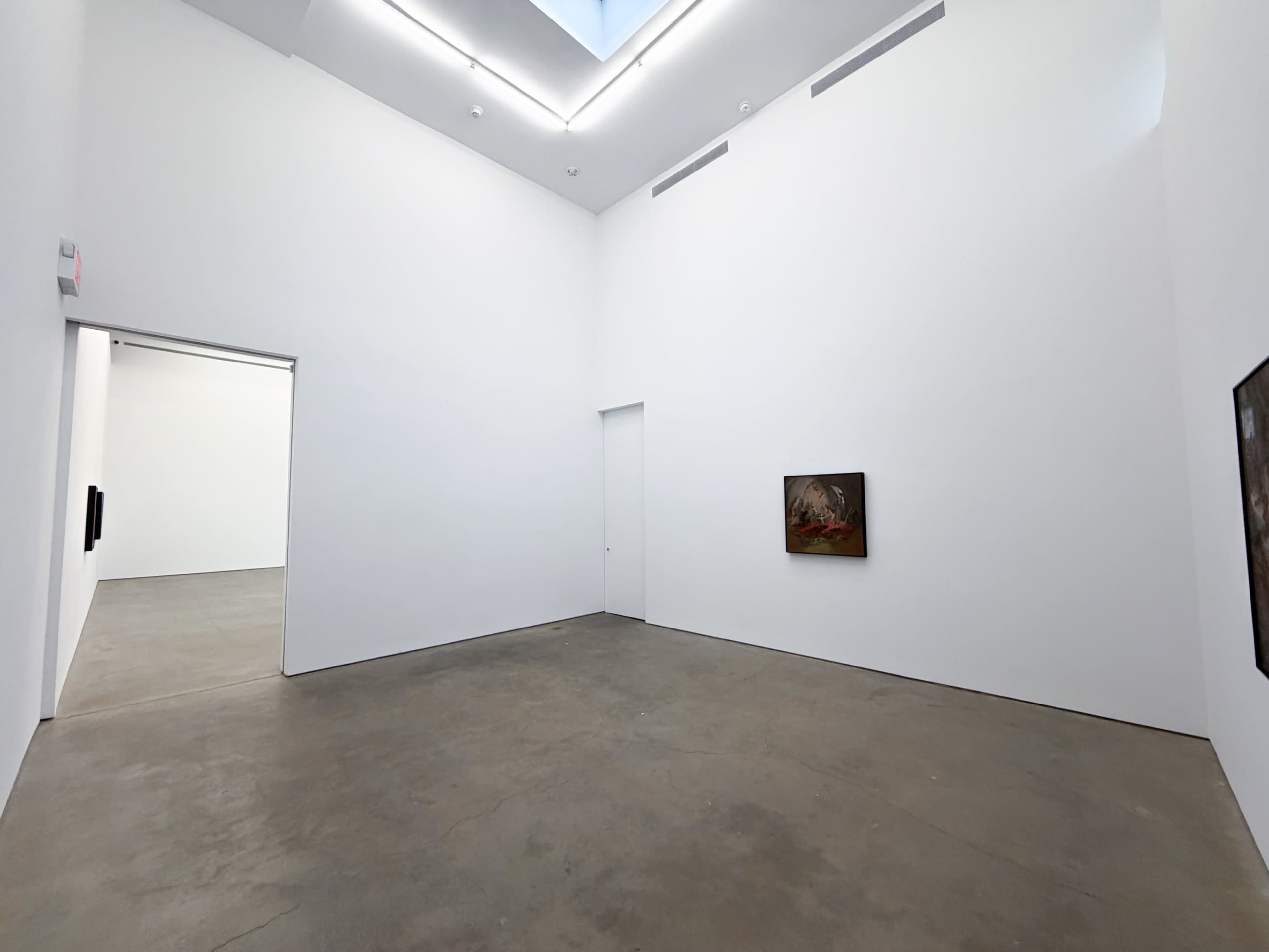 The image shows a spacious, minimalist gallery with white walls and a concrete floor, featuring two paintings, one visible on the right and a doorway leading to another room on the left.