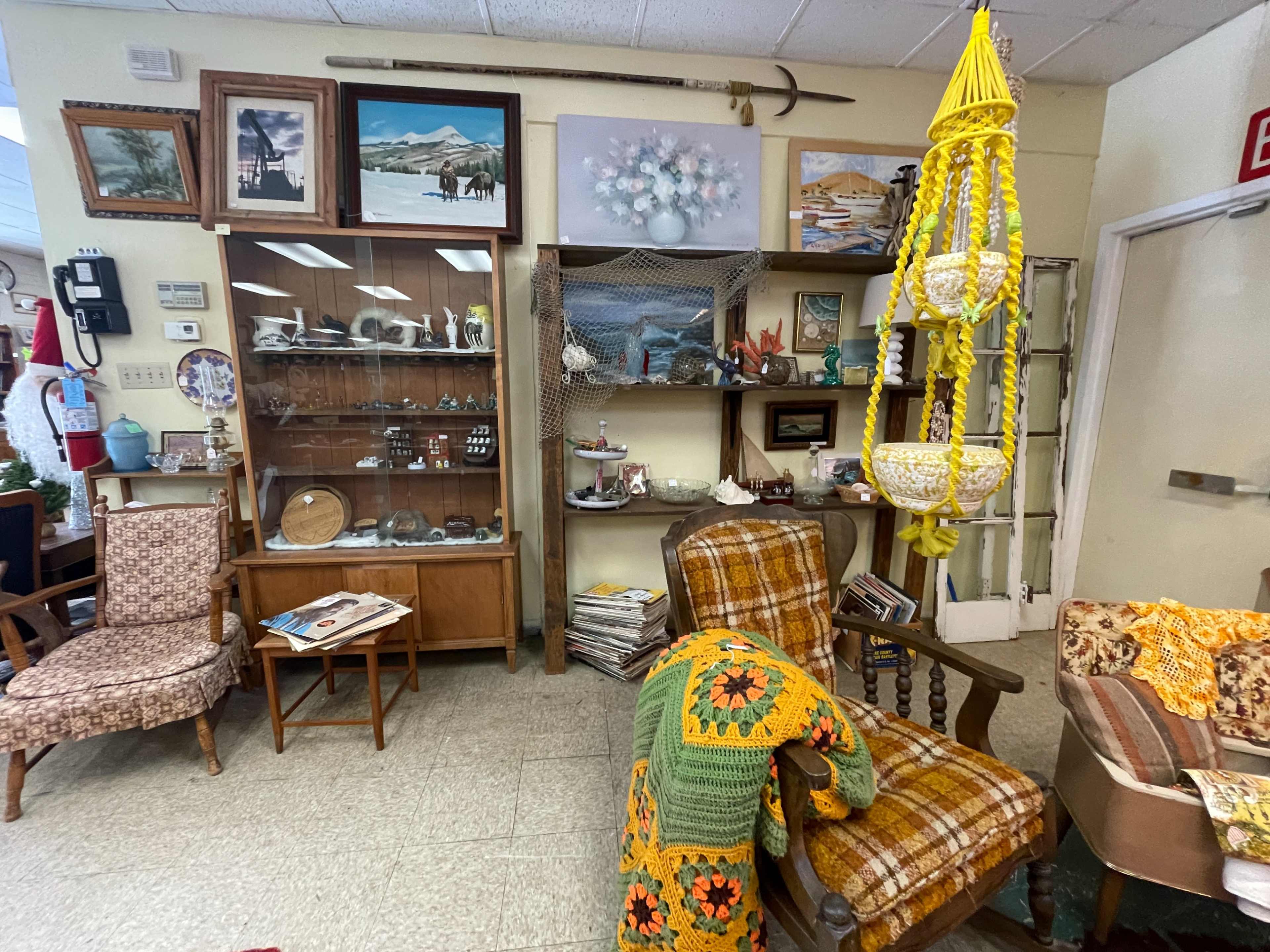 The image shows a vintage shop interior featuring shelves filled with various collectibles, a patterned chair, and a hanging decorative item.
