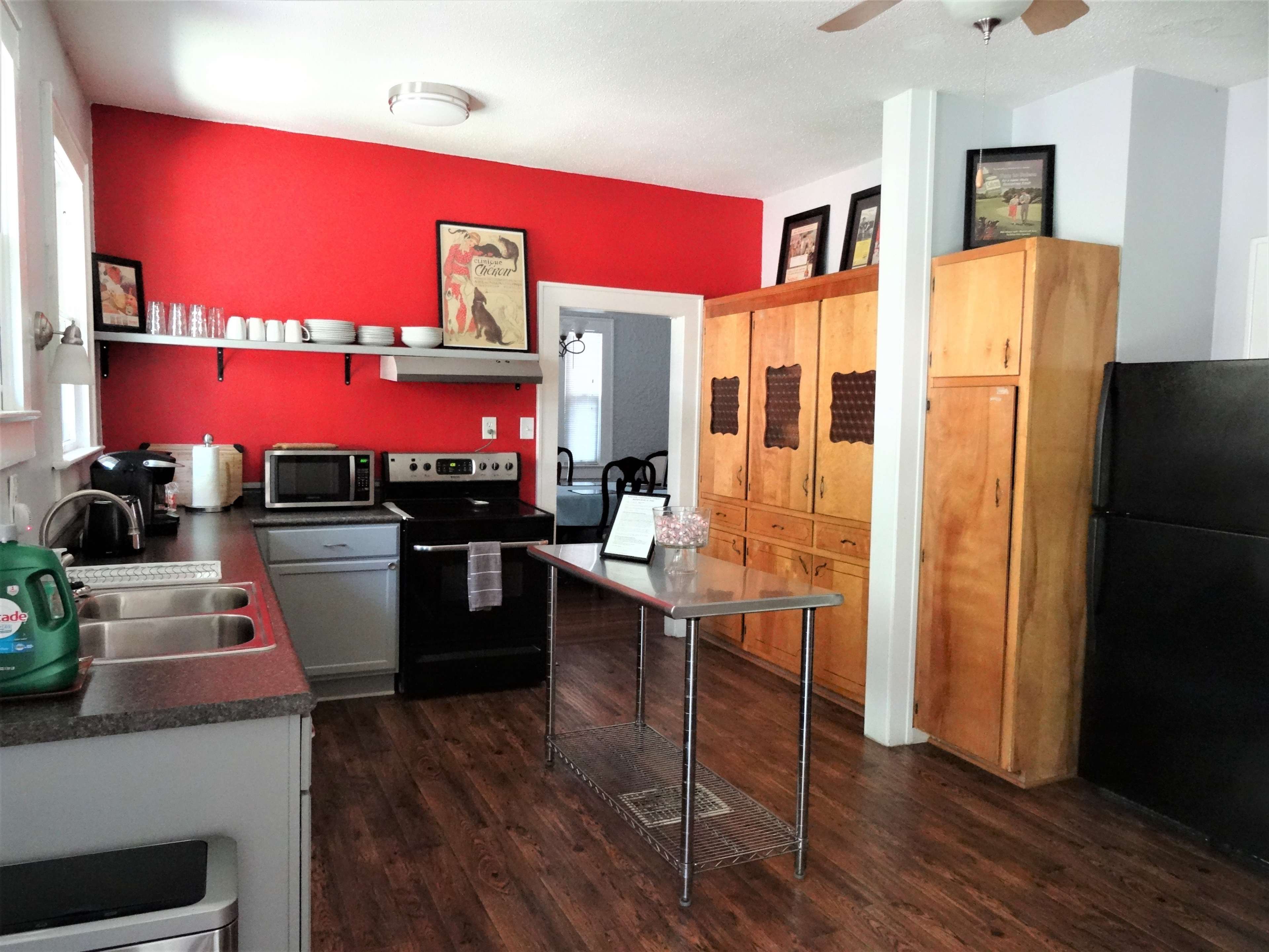 The image shows a kitchen with a red accent wall, stainless steel appliances, a central island, and wooden cabinets.