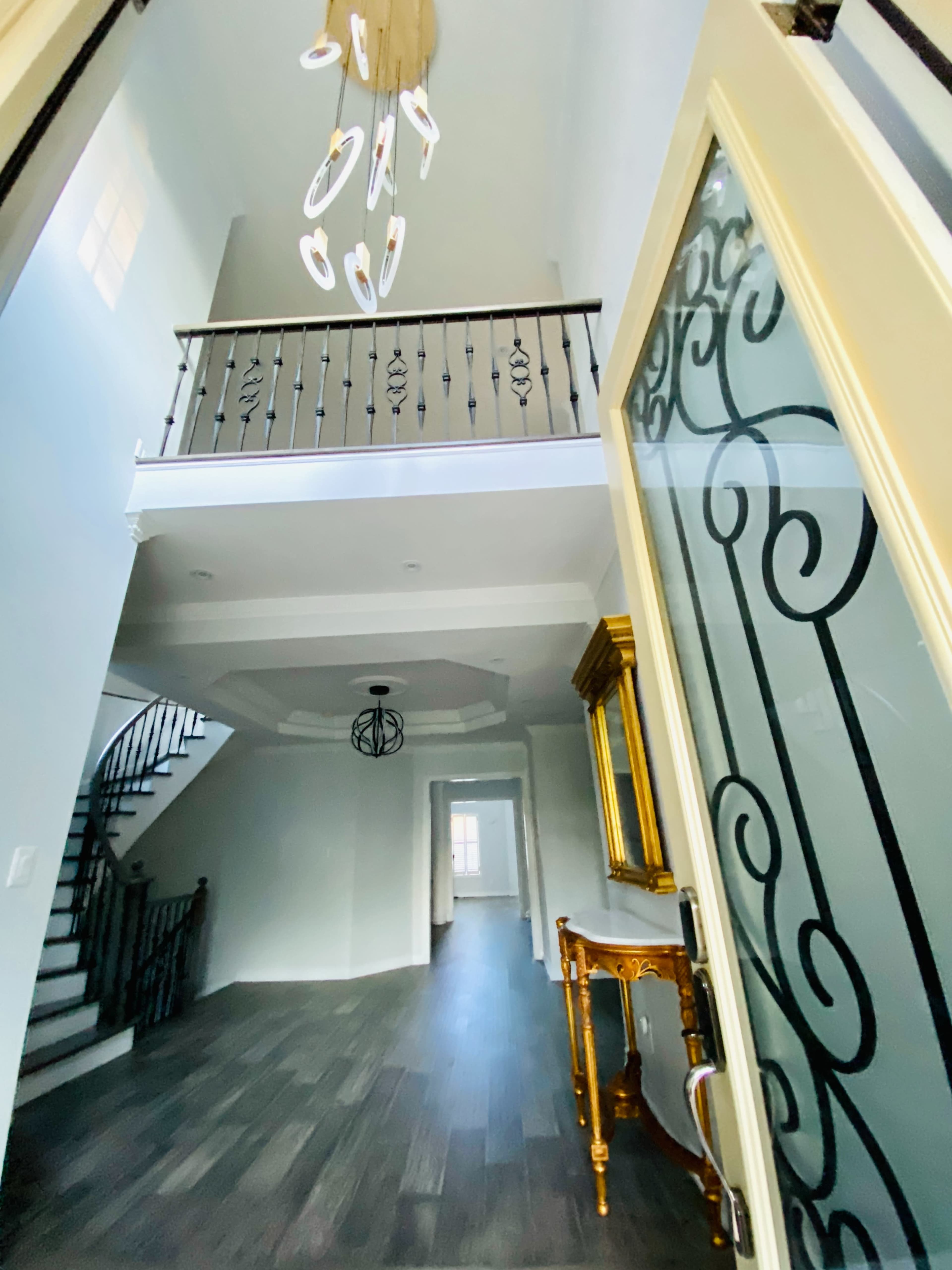 A spacious entryway features a staircase, a chandelier, and decorative railings leading to an upper level.