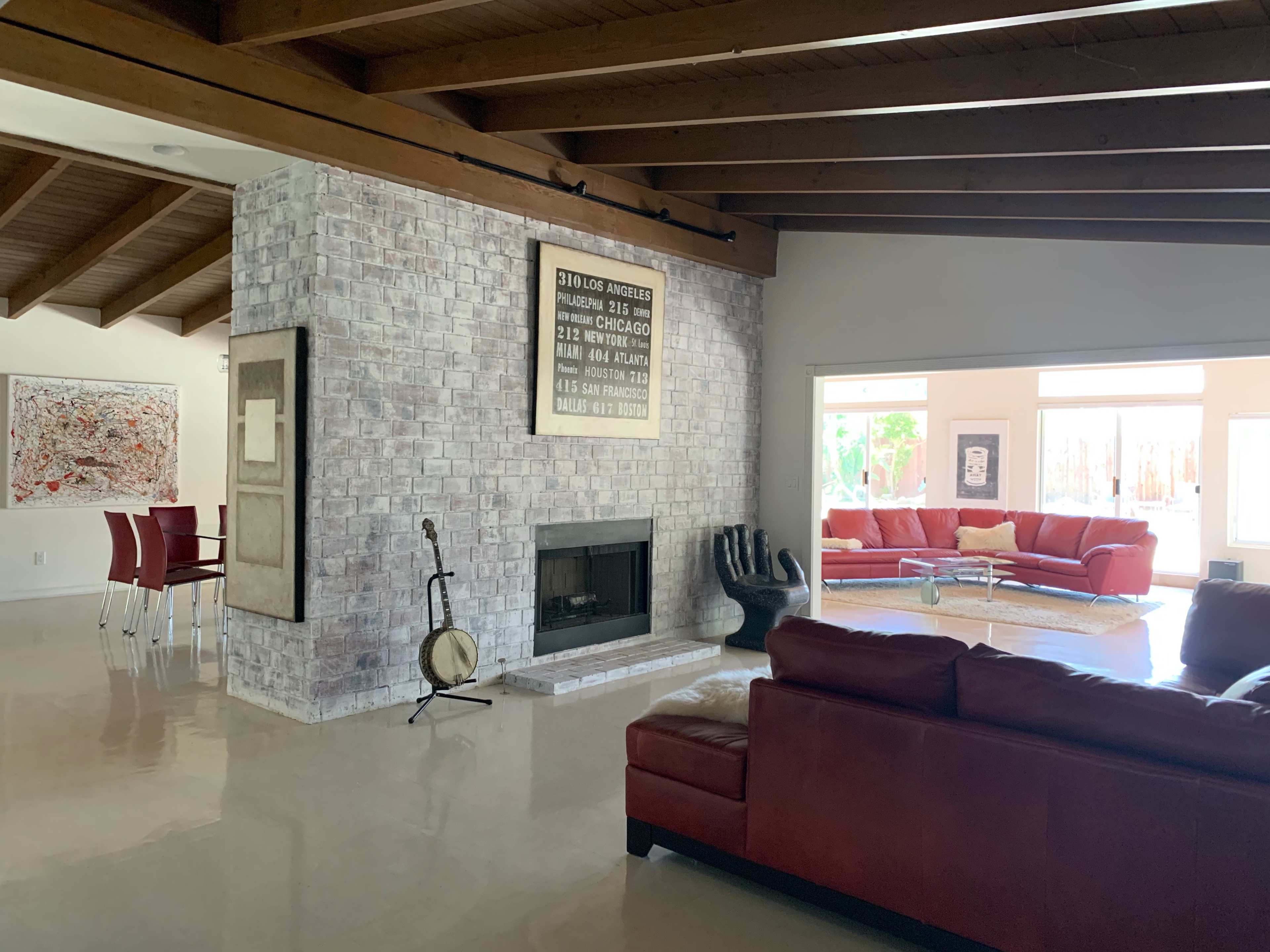 A modern living space with a red leather sofa, a brick fireplace, and a dining area featuring a glass table and four chairs.