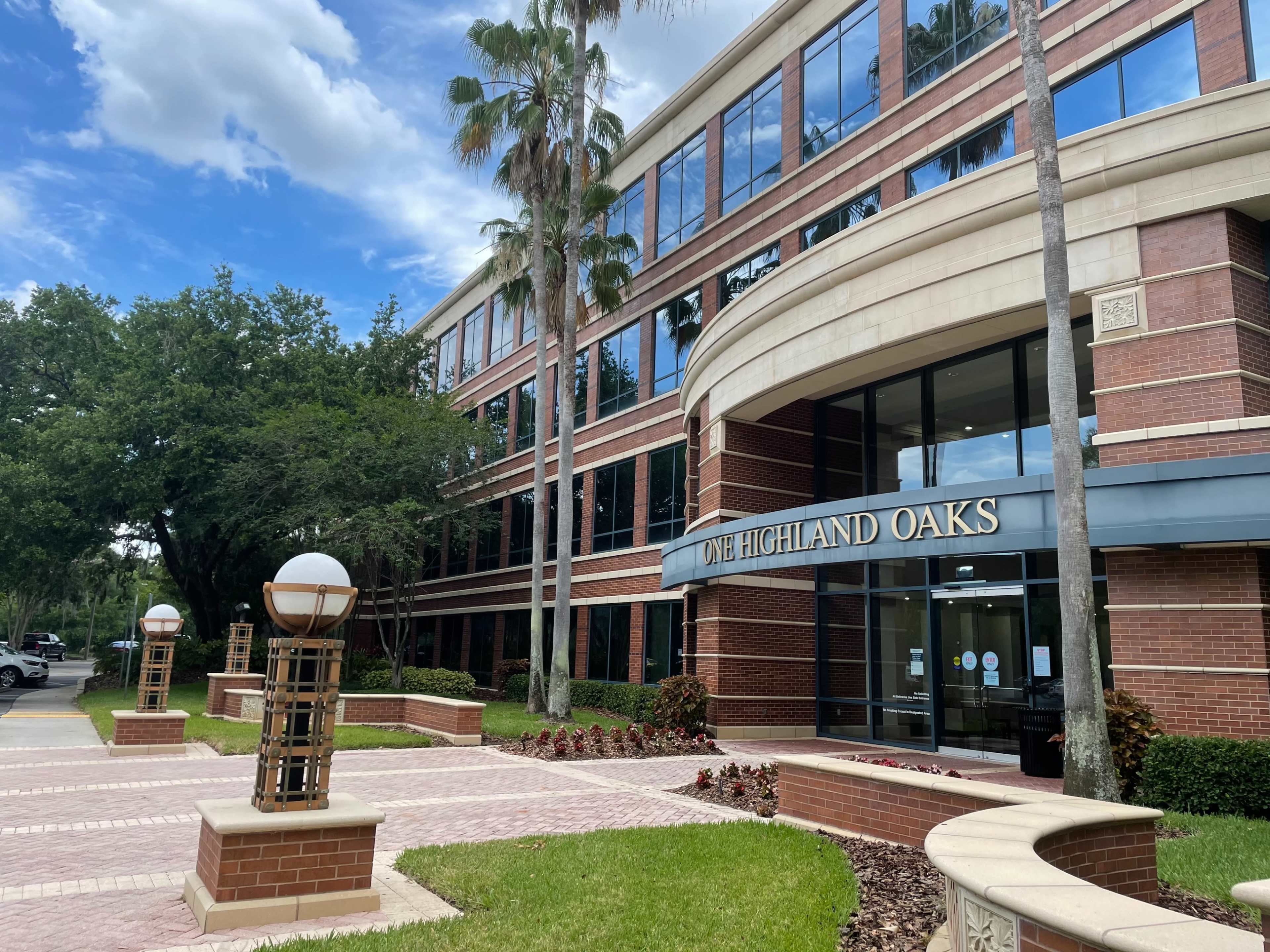 A multi-story brick office building with large windows and landscaping featuring palm trees and decorative light fixtures.
