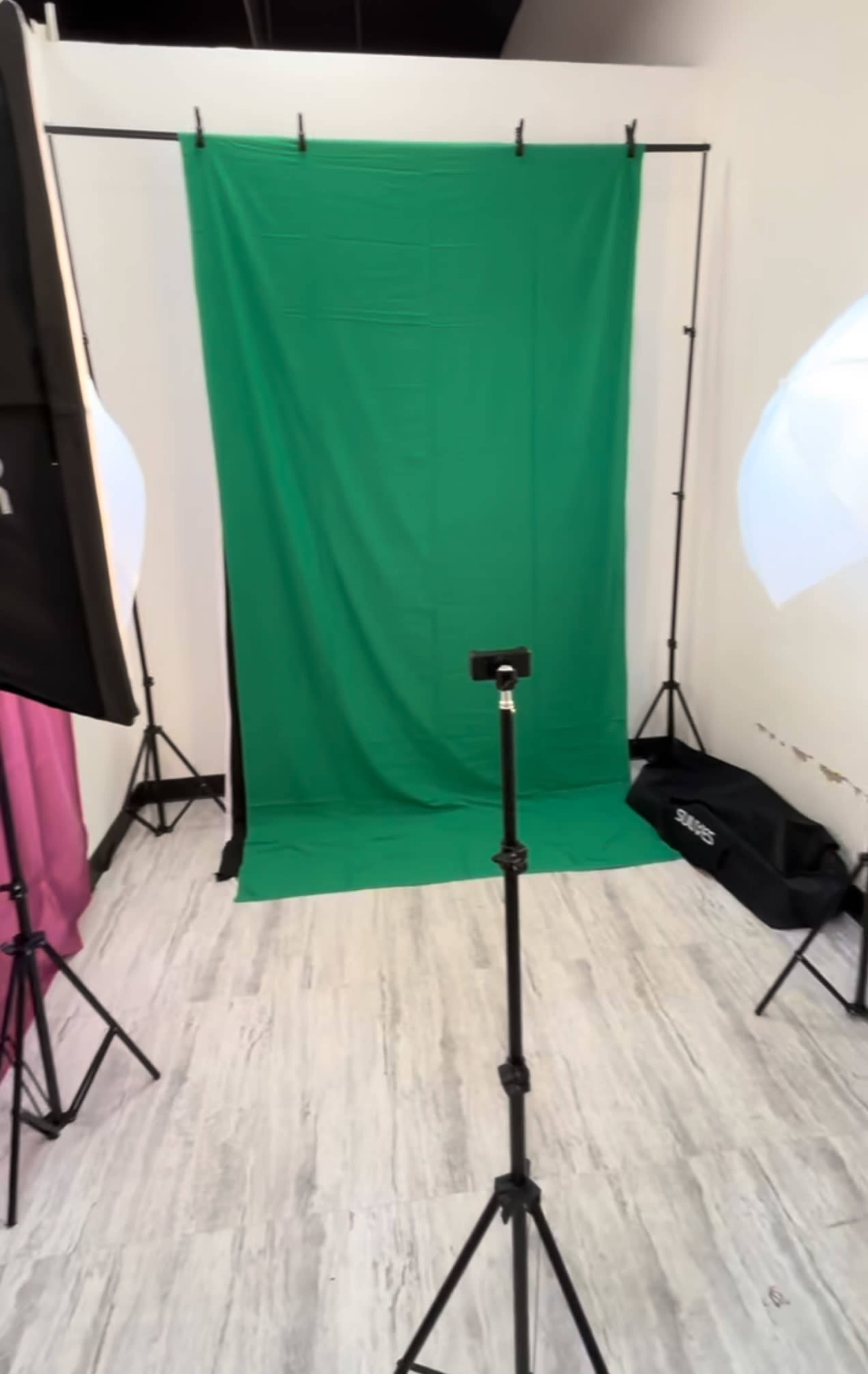 The image shows a studio setup with a green backdrop, a camera on a tripod, and lighting equipment arranged around the scene.