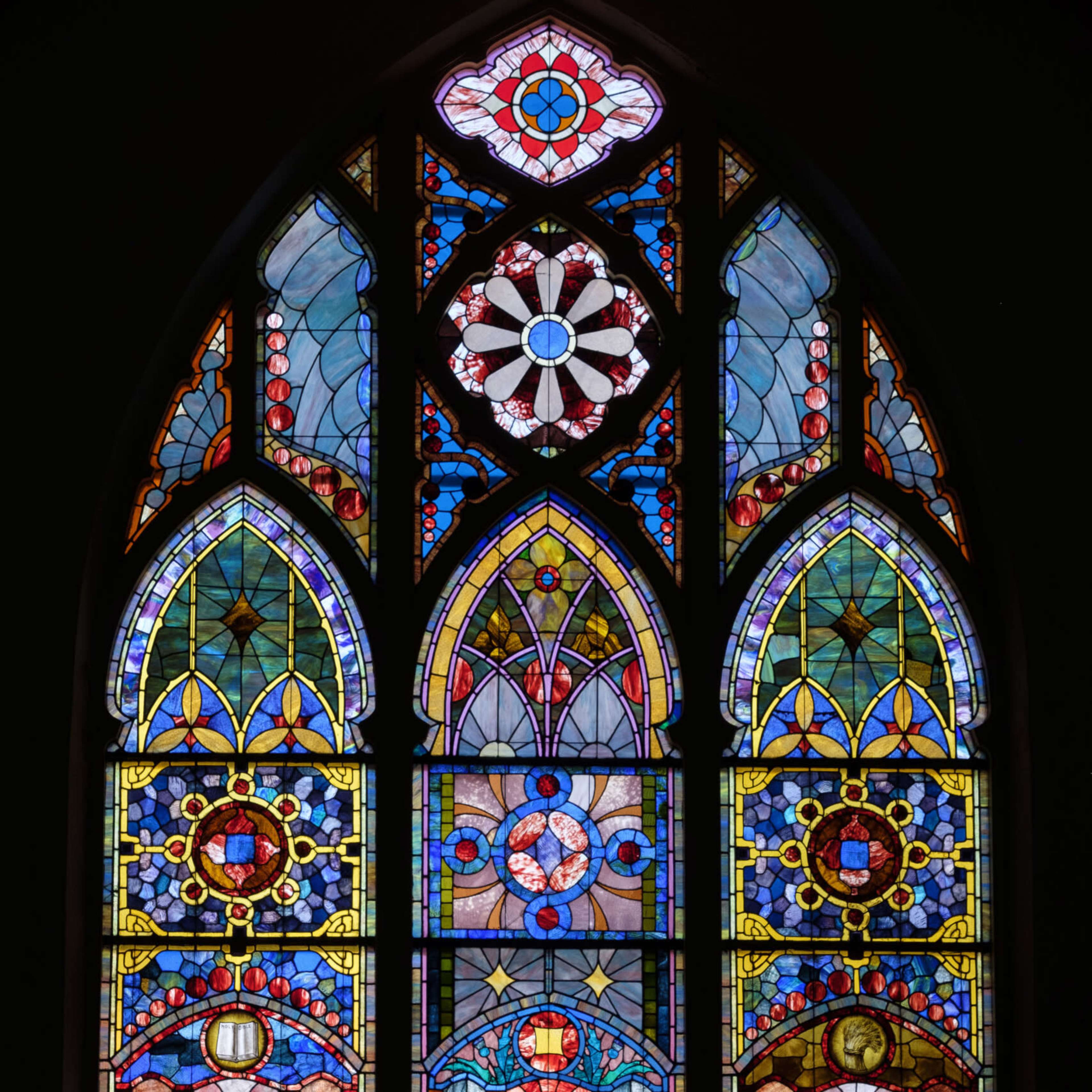 A Gothic-style stained glass window featuring intricate geometric patterns and colorful designs.