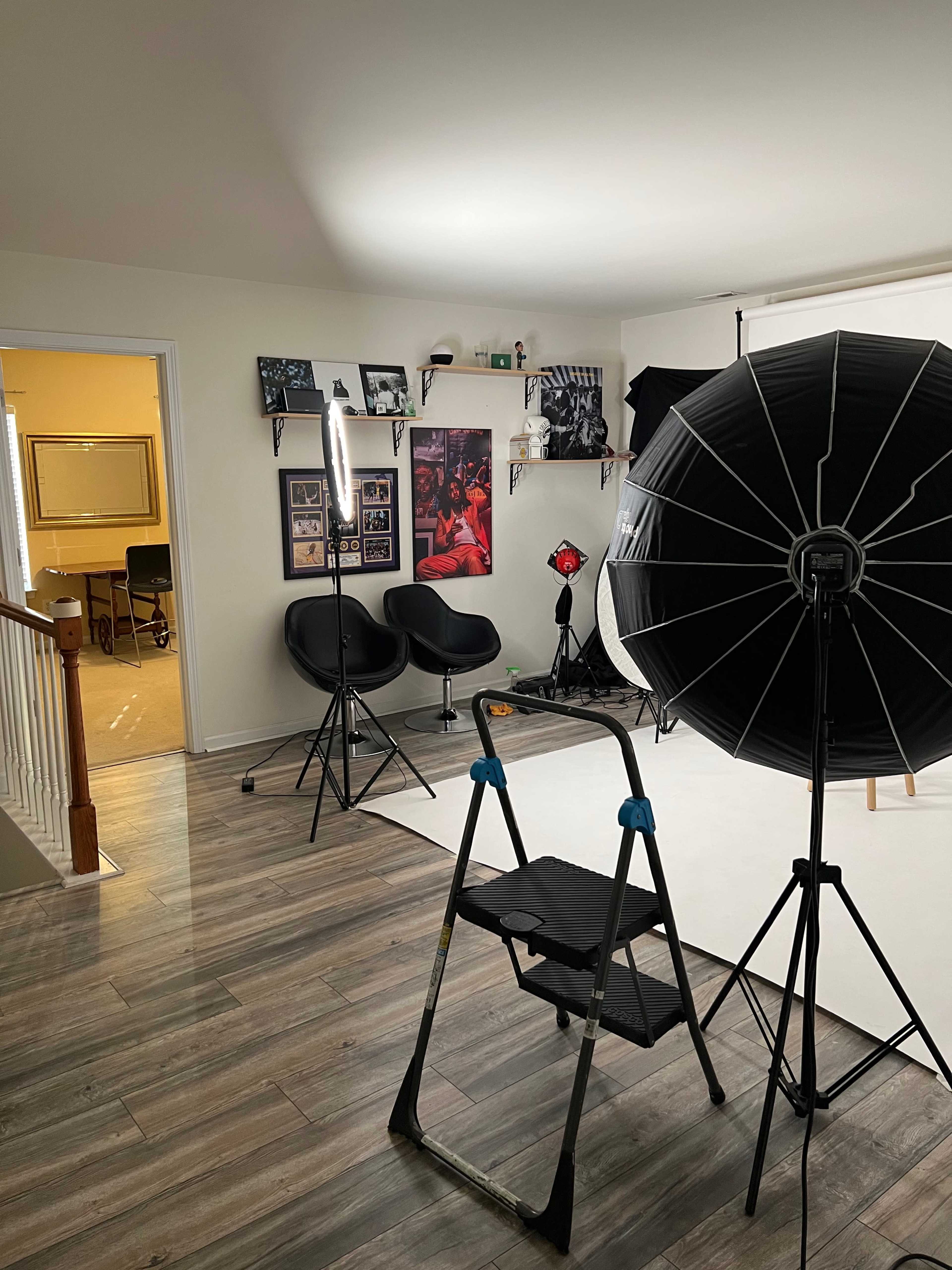 A photography studio setup featuring lighting equipment, a ladder, and framed photos on the walls.