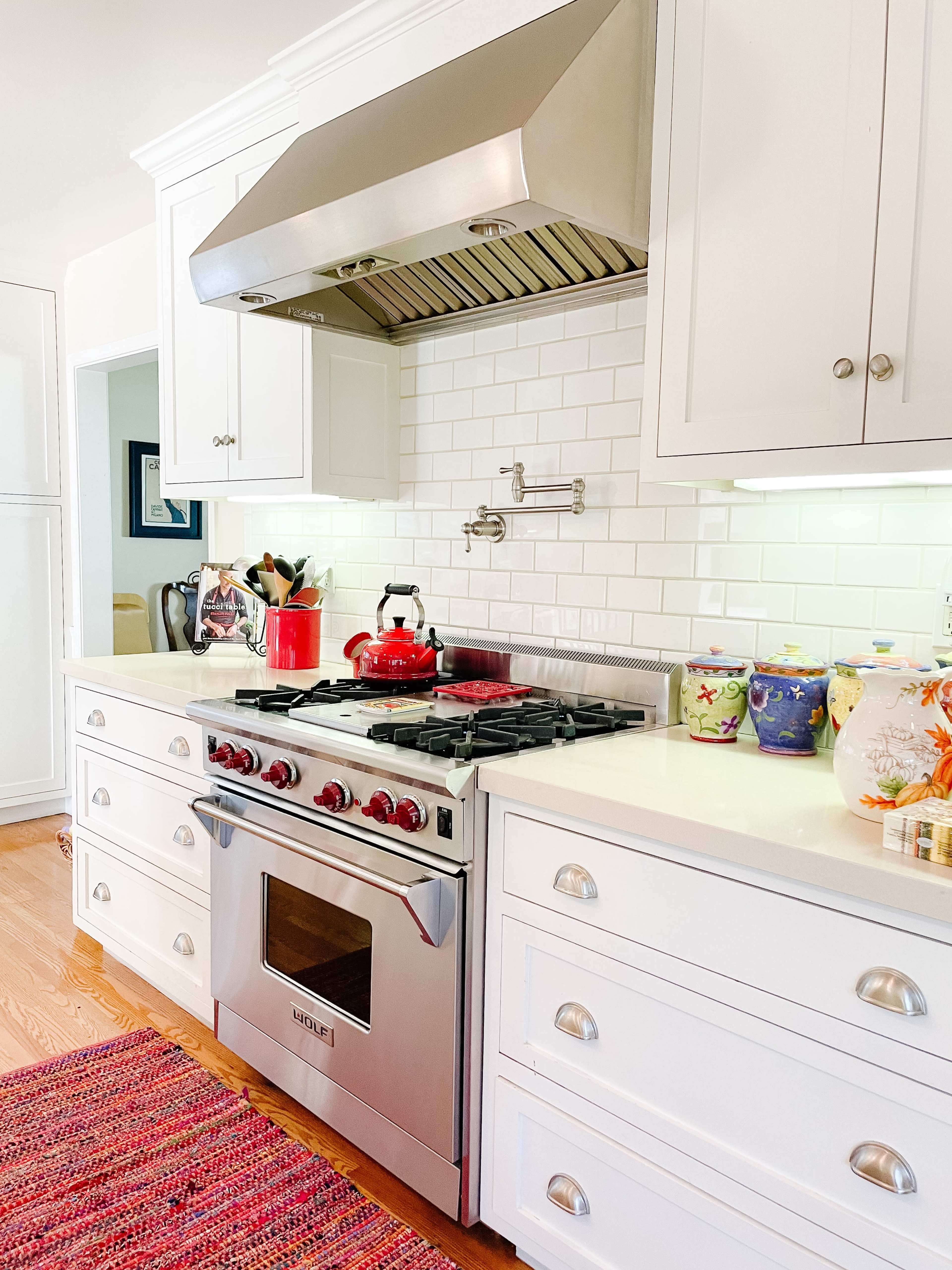 The kitchen features white cabinetry, a stainless steel gas stove with a red kettle, and colorful dishware displayed on the counter.