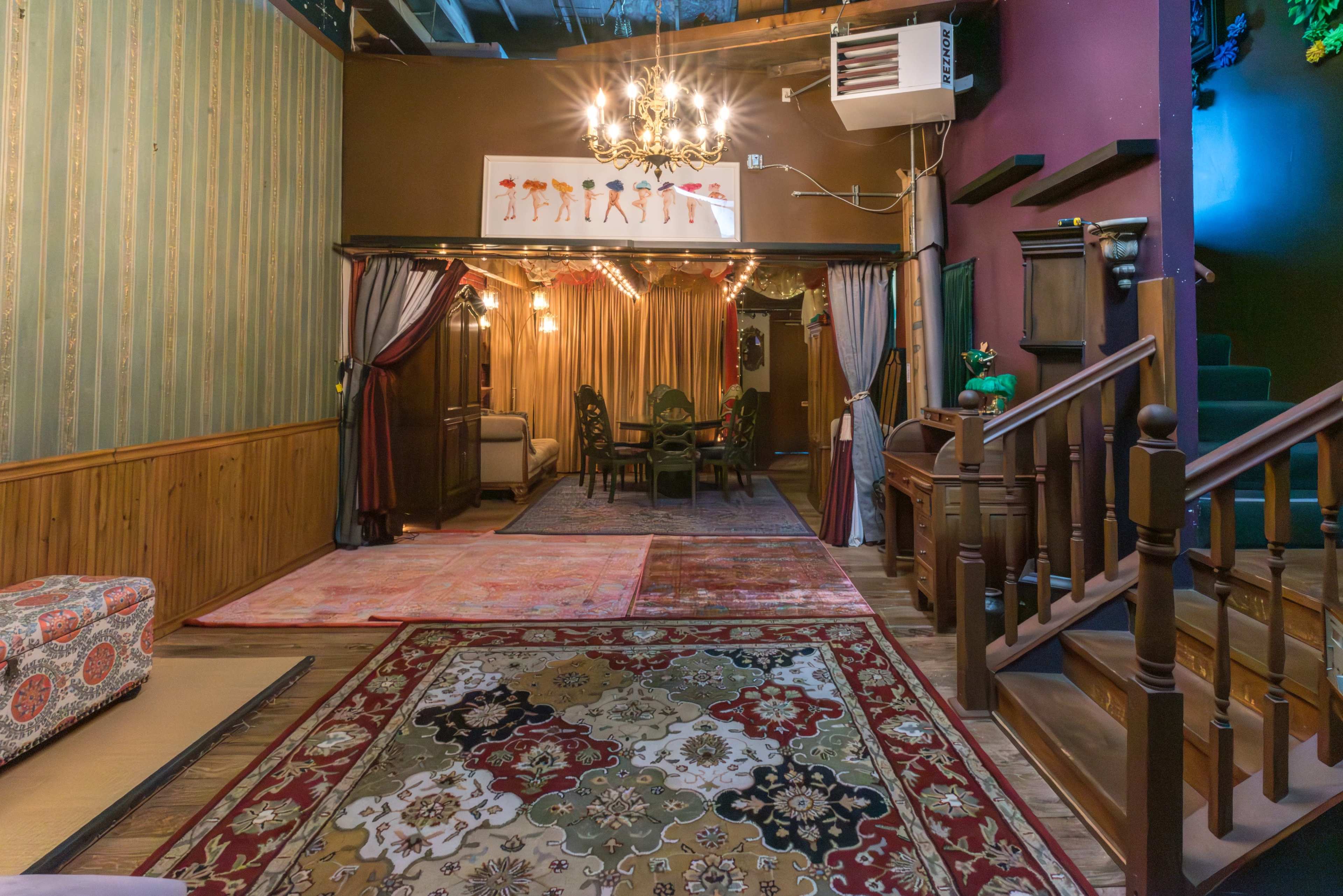 An interior room featuring a patterned carpet, a chandelier, and a dining area with a table and chairs, surrounded by ornate decor and warm lighting.