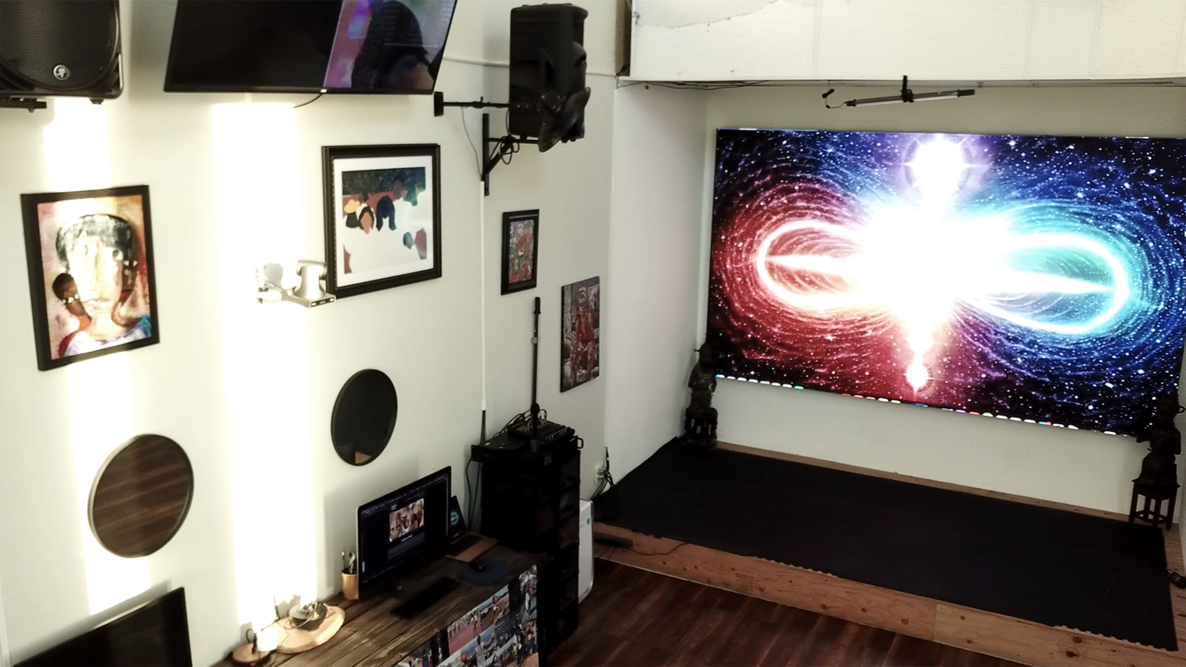 The image shows a modern, well-lit room with a large colorful display on one wall, surrounded by various artworks and decorative elements.