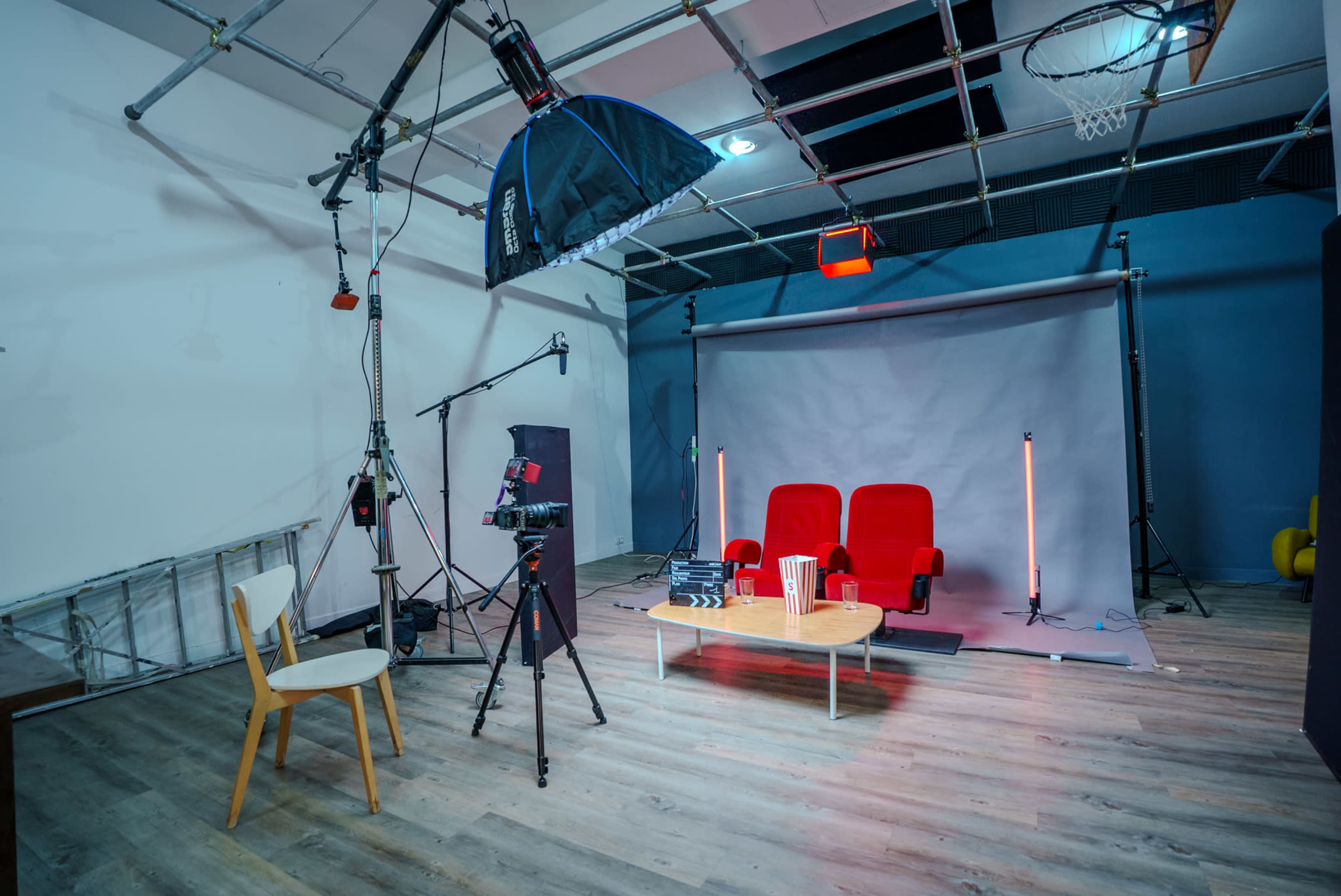 A photography studio is arranged with two red chairs, a wooden table with popcorn, and various lighting equipment set up for a shoot.